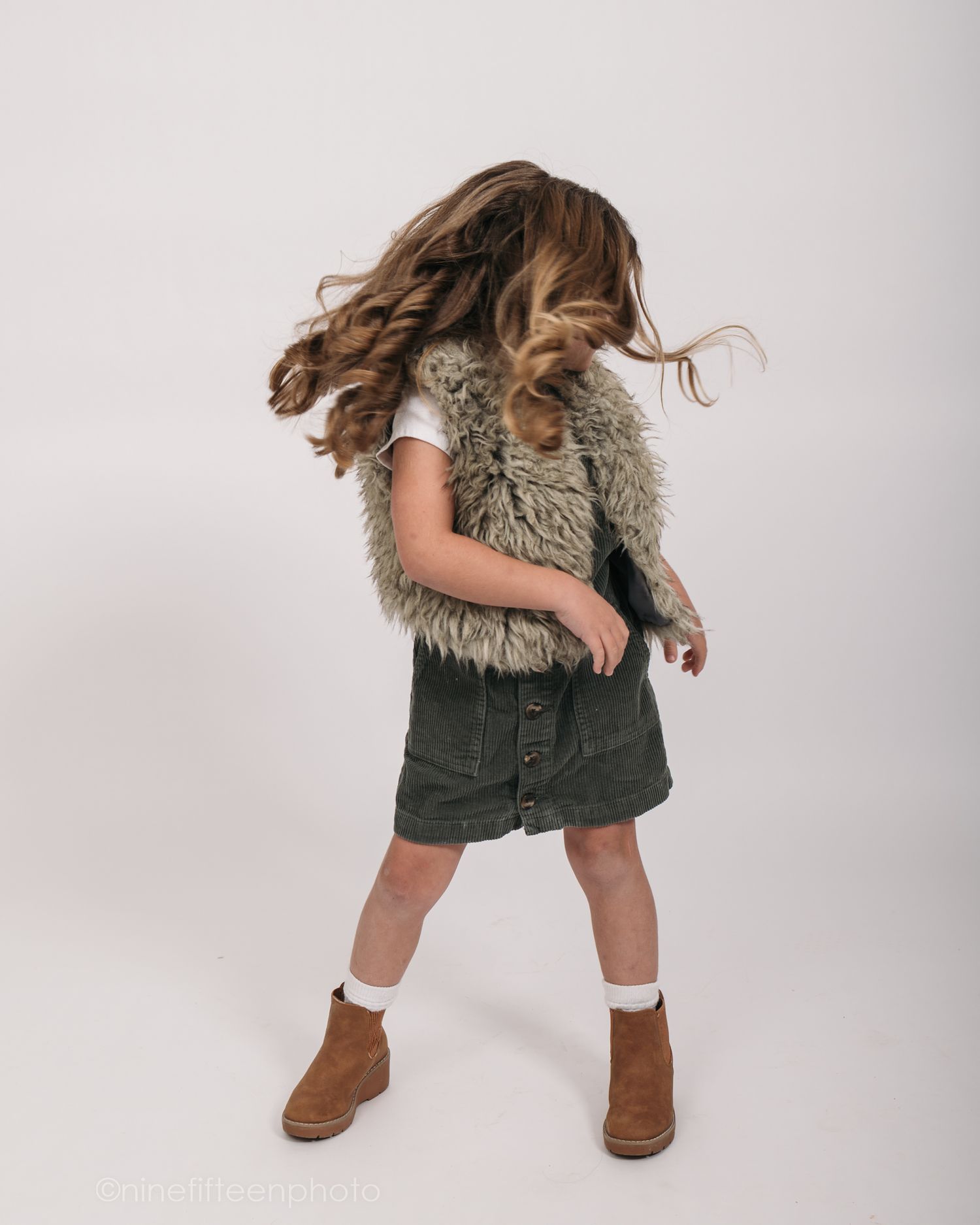 Studio personality portrait of a young girl smiling confidently in a textured vest against a neutral studio backdrop in Meade County KY
