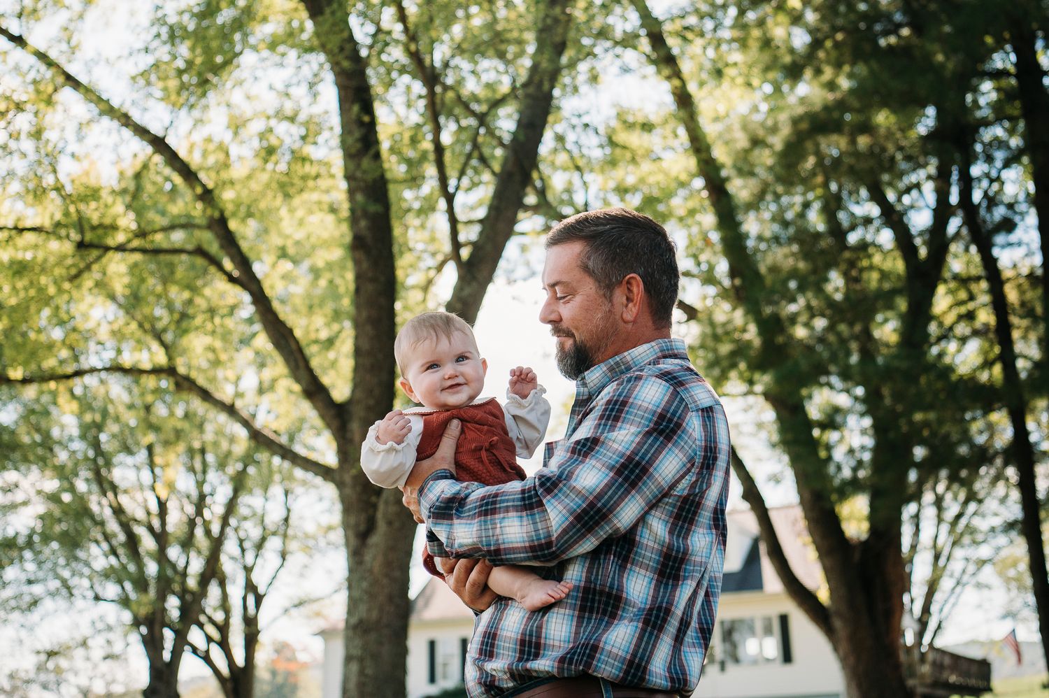 Candid outdoor photo of dad holding baby during a Battletown KY farmhouse family session captured by ninefifteenphoto