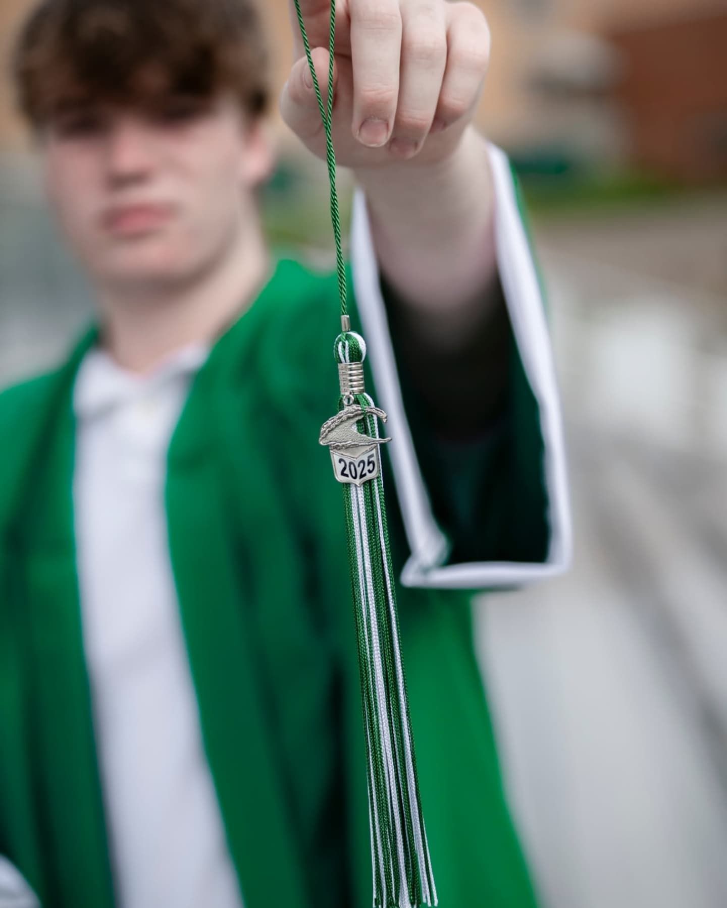 Close-up of a graduate holding a 2025 tassel in green and silver colors.