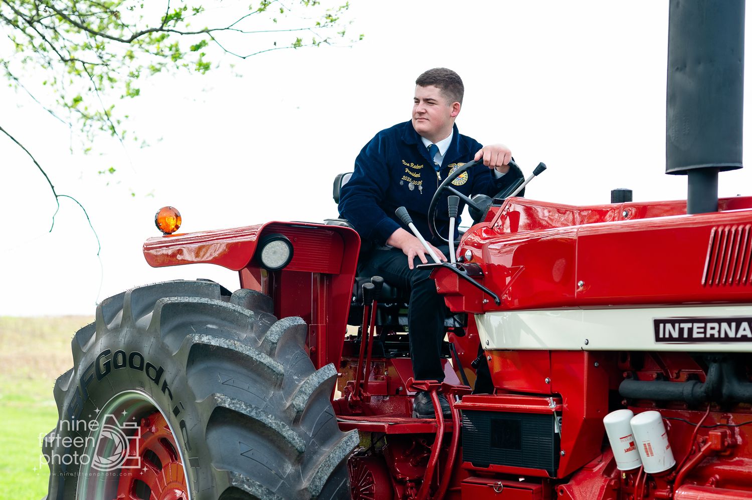 Young man in FFA jacket driving a red International tractor on a green farm field.