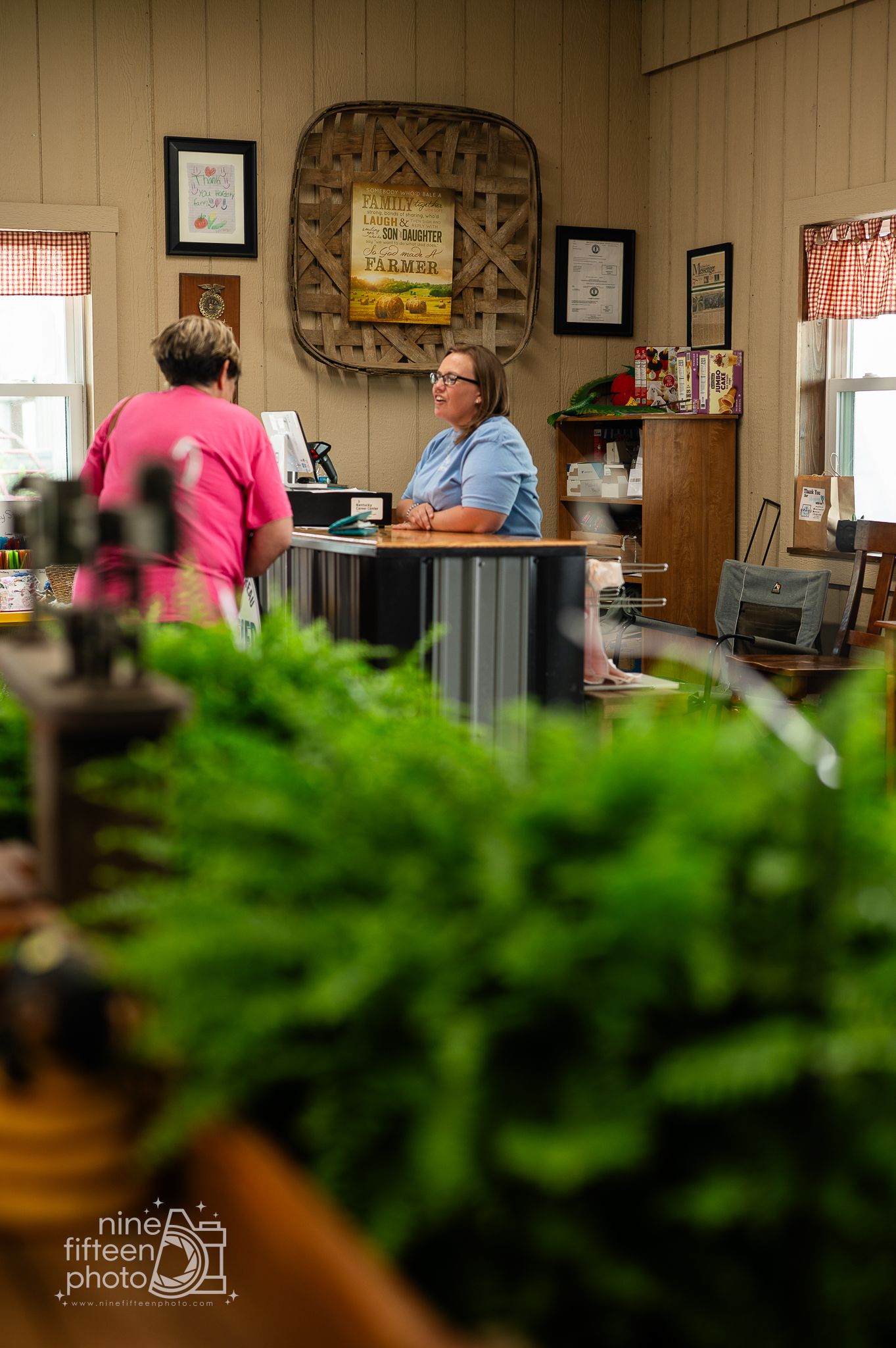 Customer and employee interacting at the counter of a rustic farm market with fresh plants.