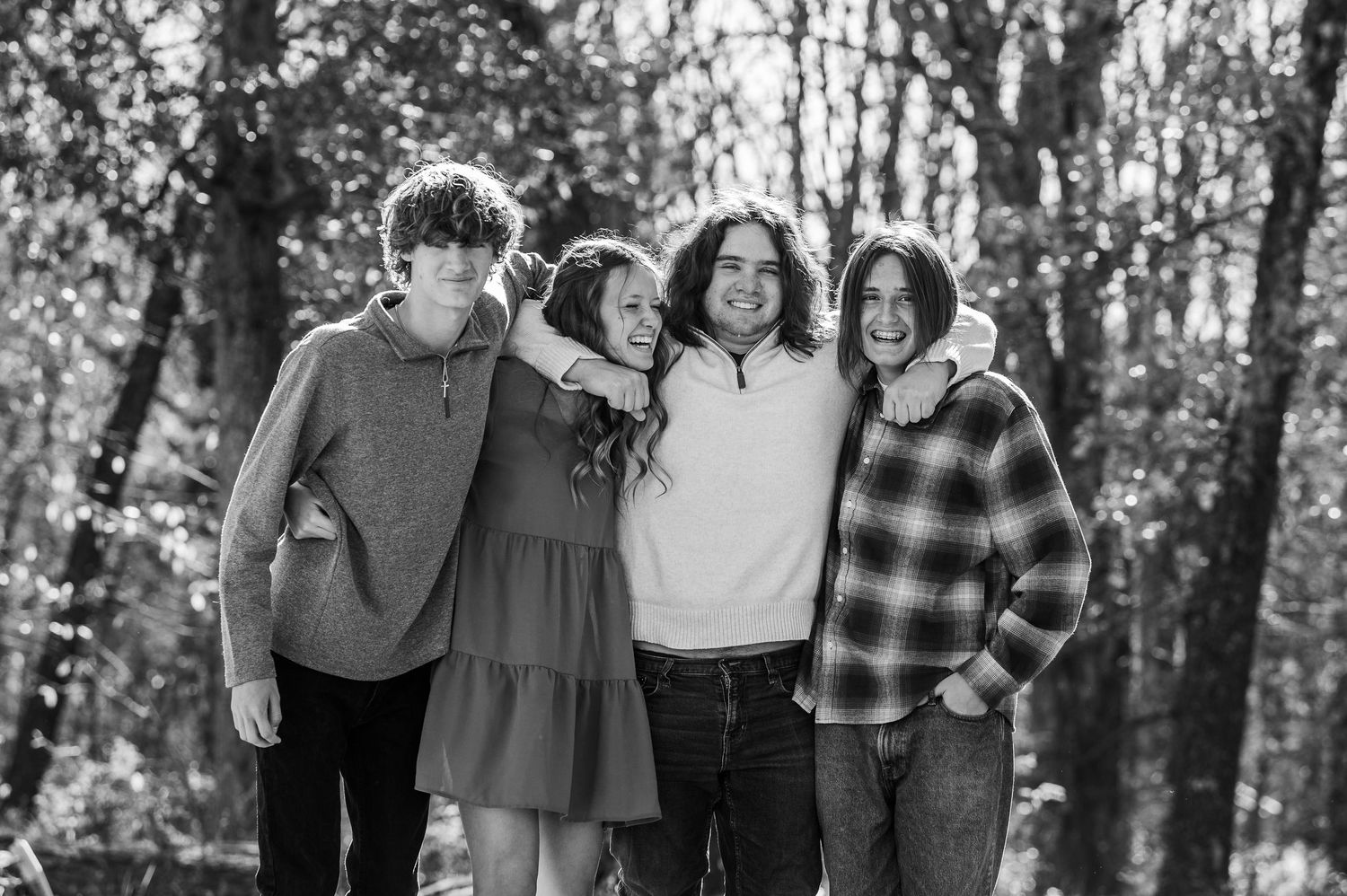 Black and white photo of four smiling teenagers posing together outdoors among trees.