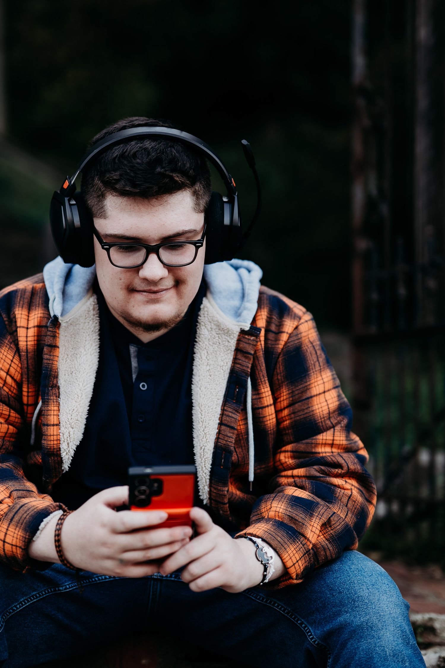 Luca’s senior photo in orange flannel and headphones, looking at his phone during his Brandenburg KY session.
