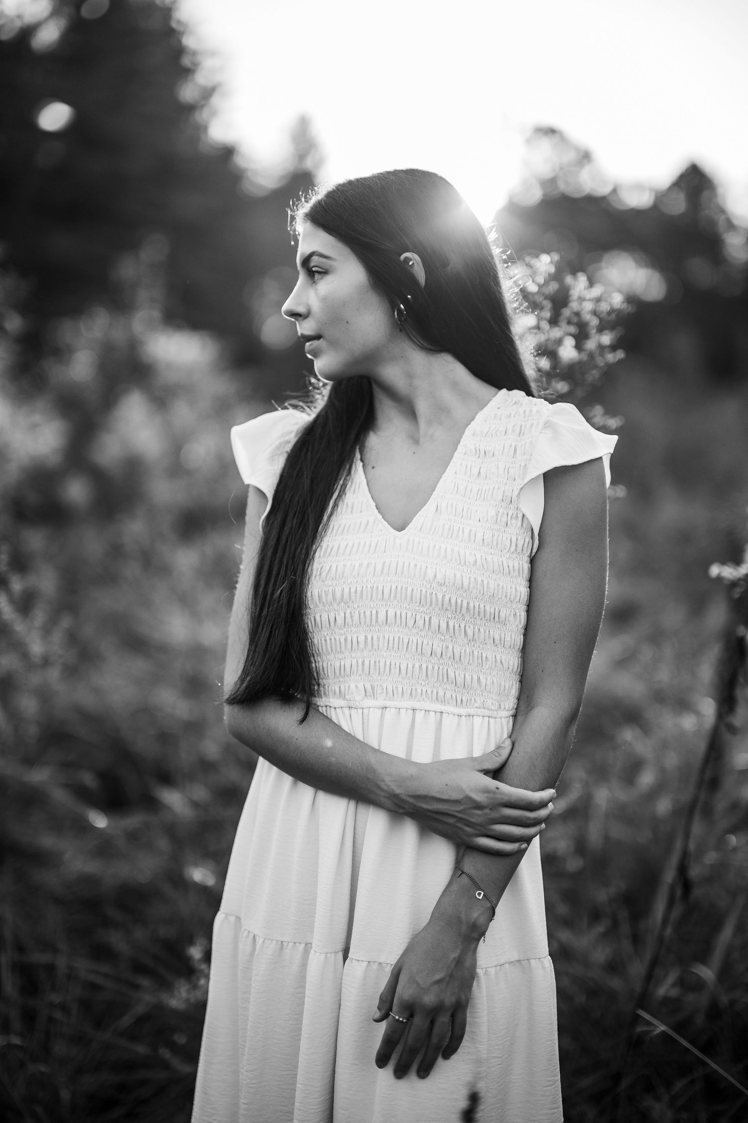 Black and white portrait of Emily in a white dress standing among trees during her senior session in Brandenburg KY.