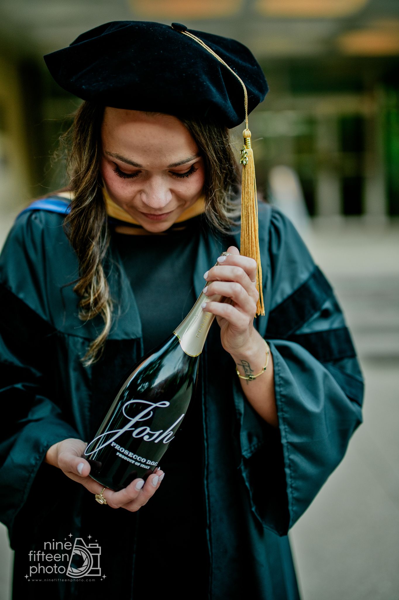 Graduate in cap and gown holding a Josh wine bottle during outdoor graduation photo session.
