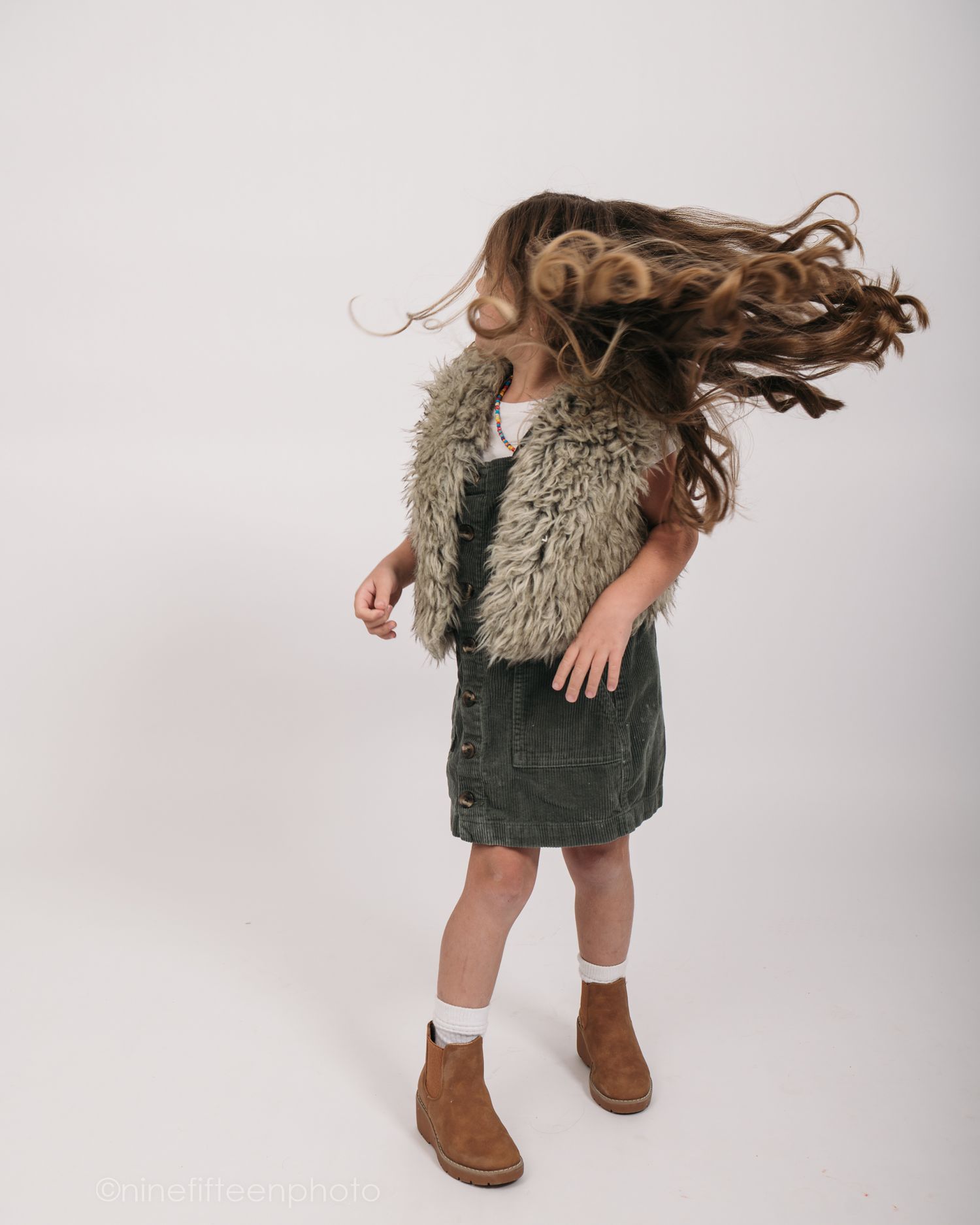 Studio personality portrait of a young girl smiling confidently in a textured vest against a neutral studio backdrop in Meade County KY