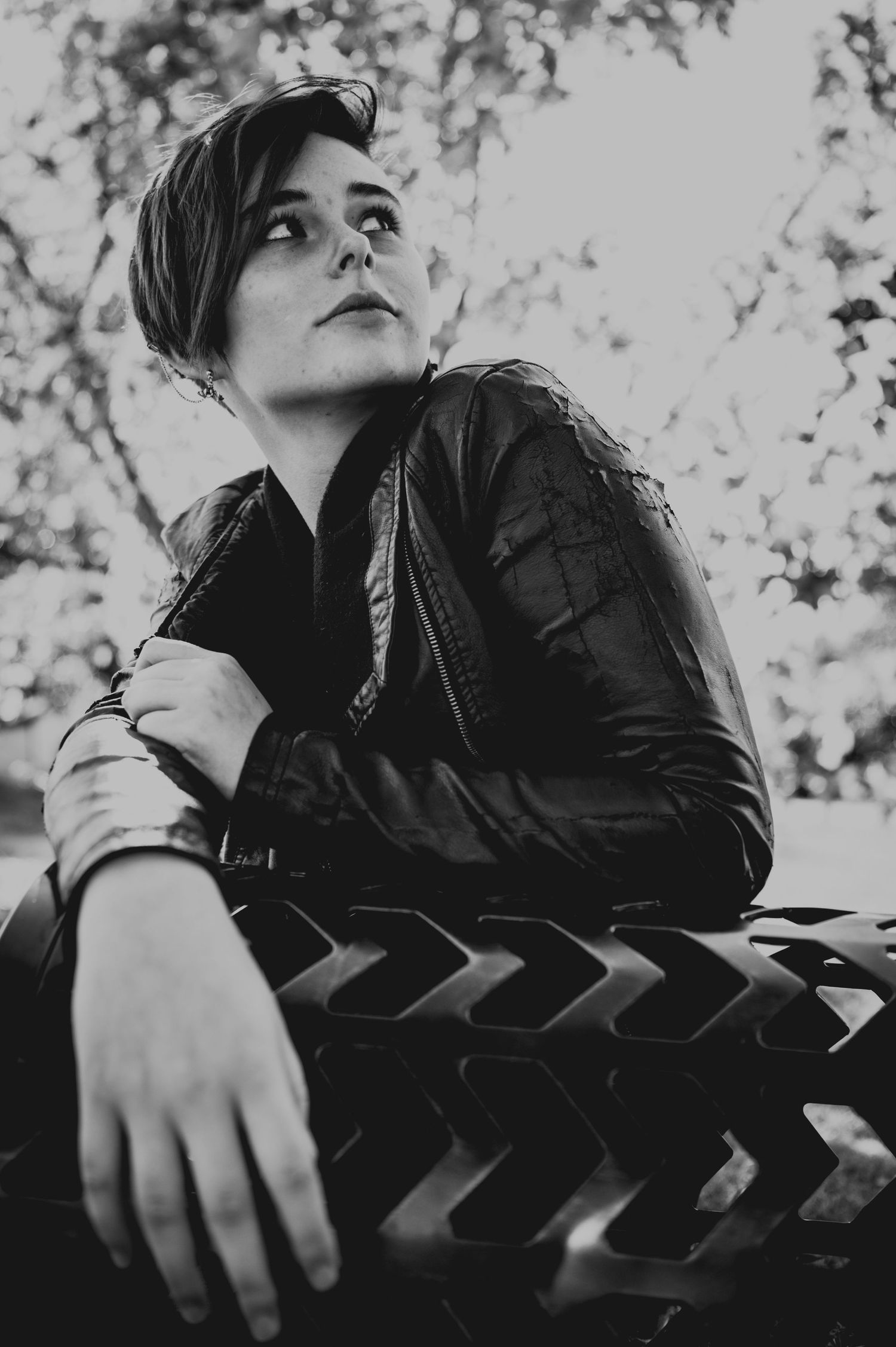 Black and white portrait of young person in leather jacket sitting outdoors.