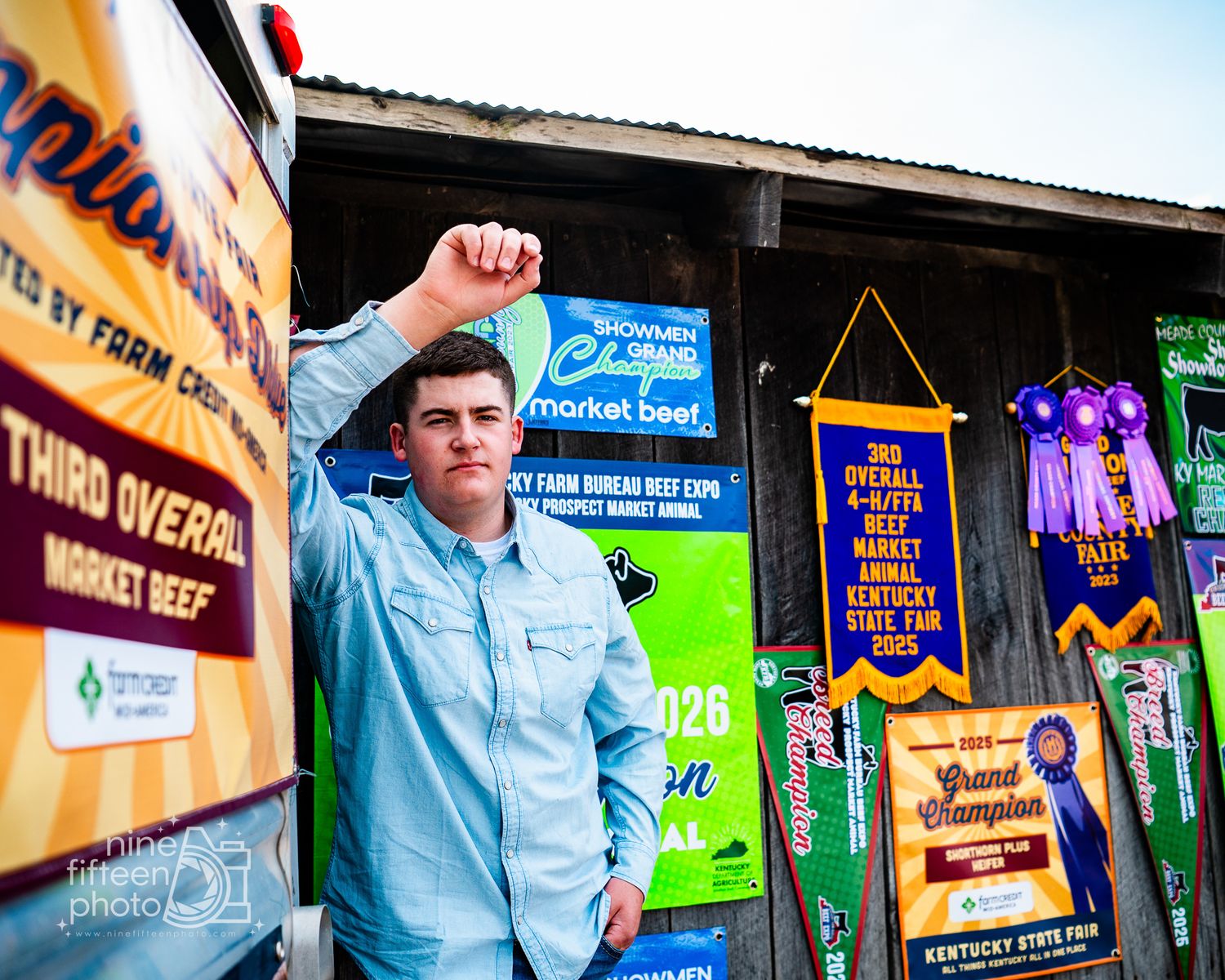 Young man raises fist in victory beside livestock show banners and Grand Champion ribbons at Kentucky State Fair.