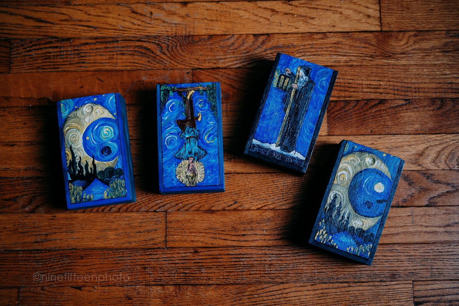 Four Van Gogh-style blue tarot card boxes with mystical figures arranged on wooden floor.