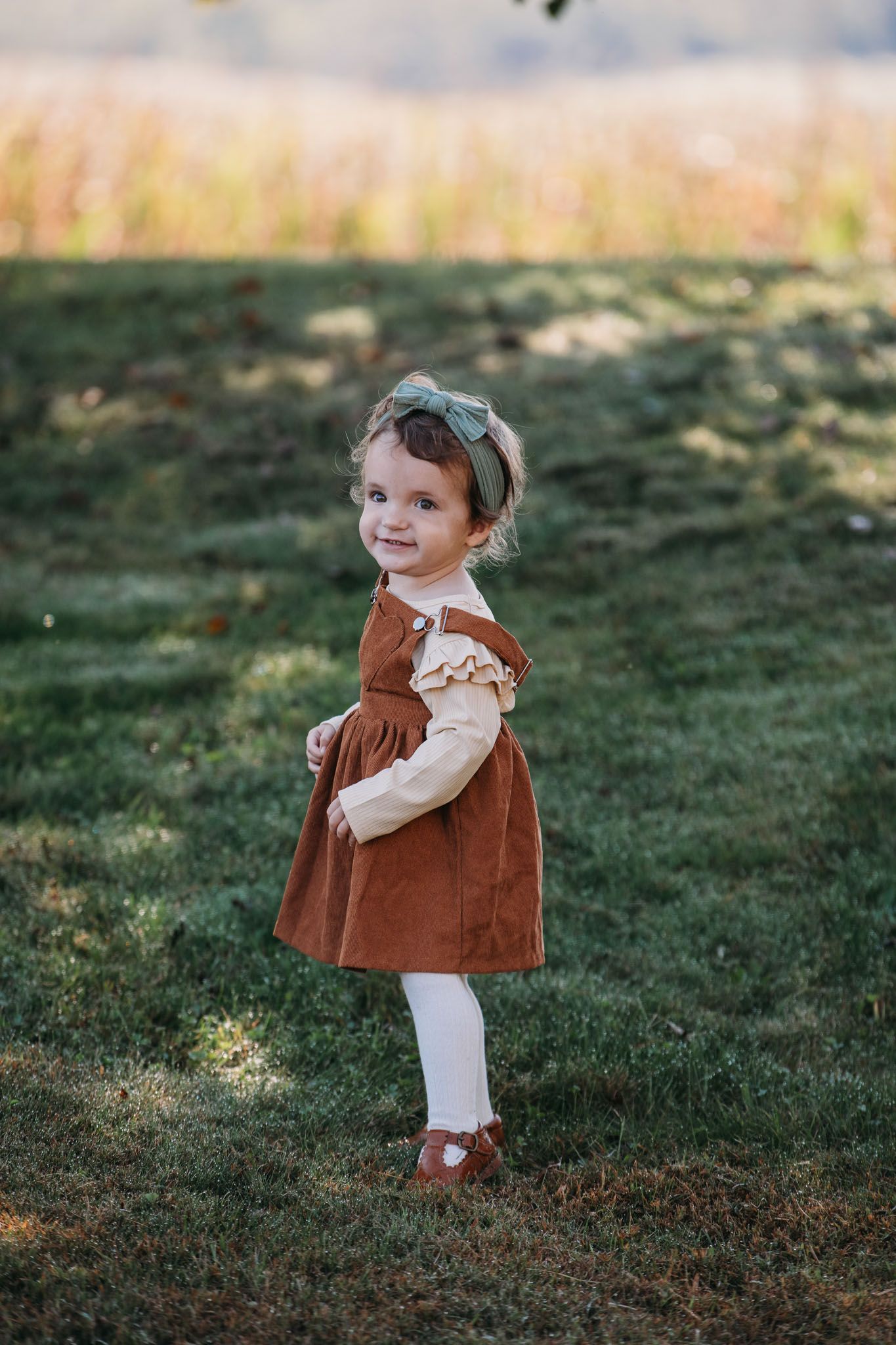 Little girl in rust-colored dress smiling in warm afternoon light during fall family portraits.