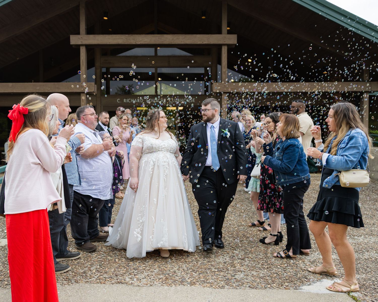 Wedding guests toss confetti over smiling bride and groom outside rustic barn venue.