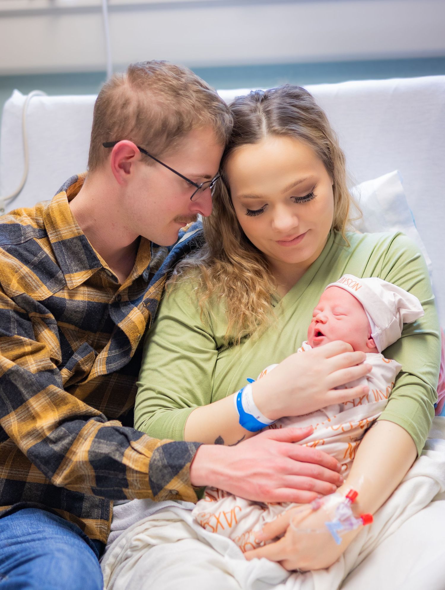 Young couple smiling and bonding with their newborn baby in a hospital room.