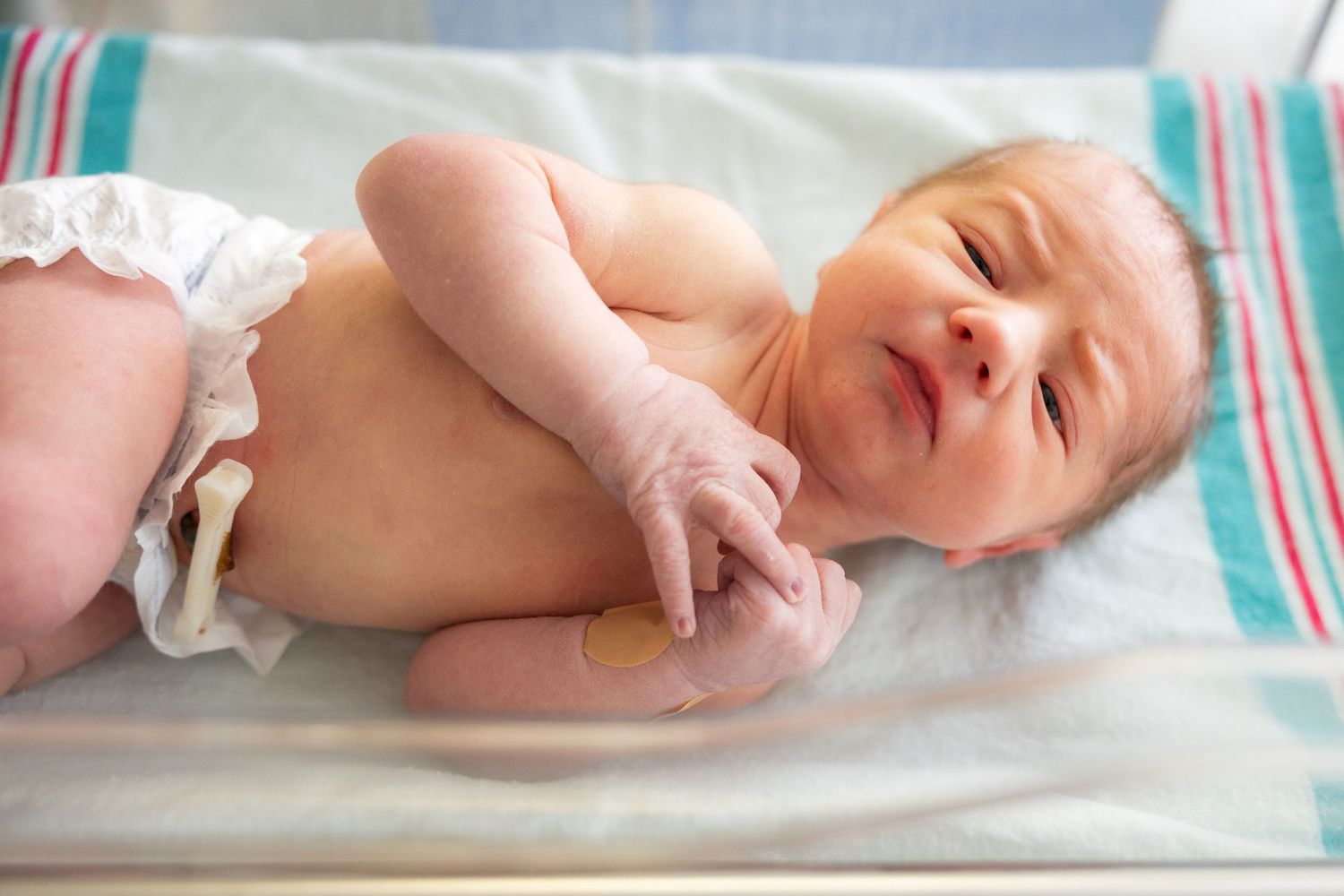 Newborn baby lying on a hospital blanket with a small bandage on their arm.