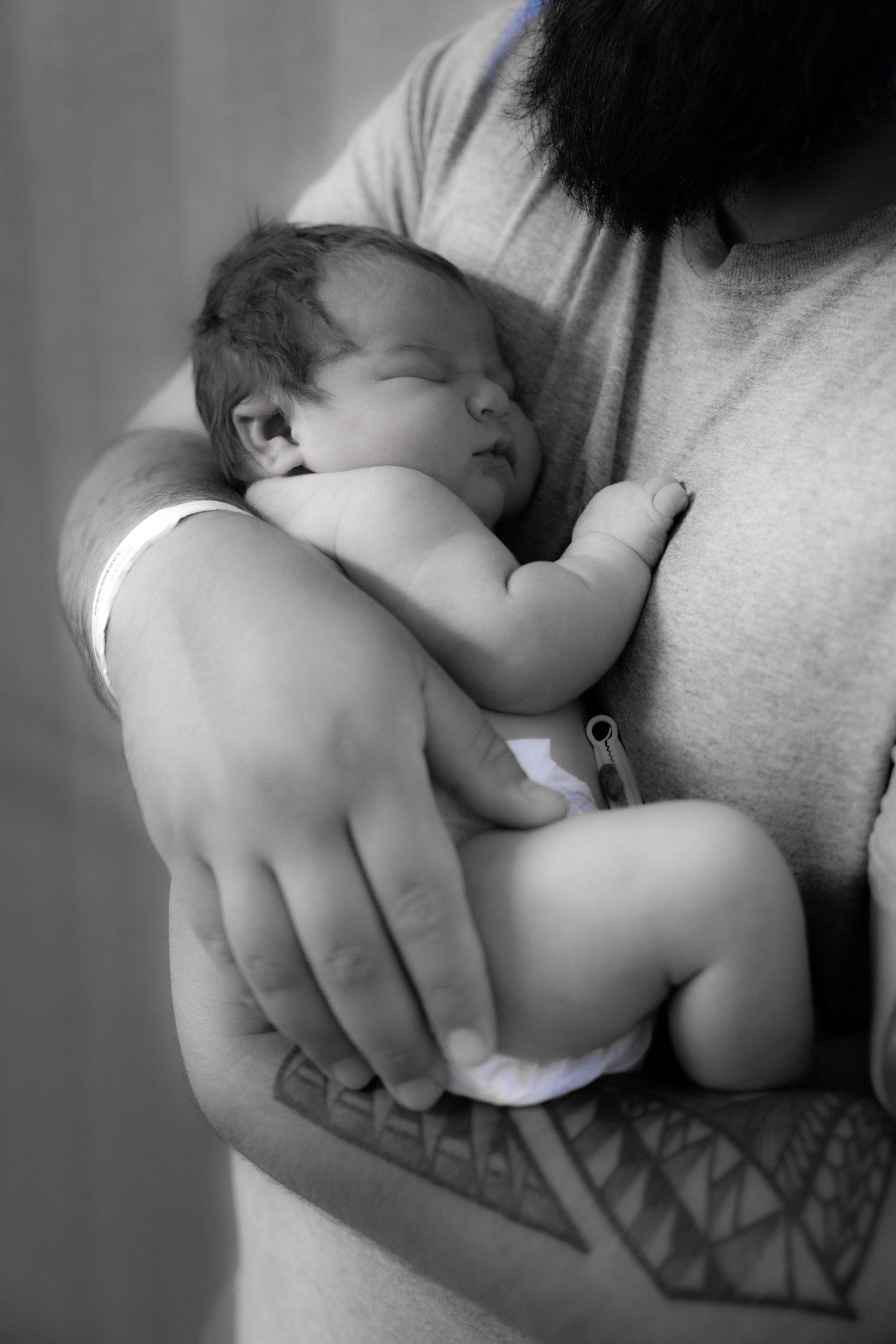 Black and white photo of a parent cradling a sleeping newborn baby against their chest.