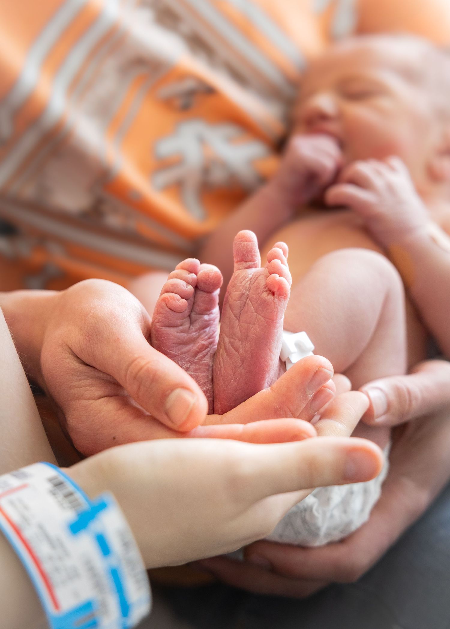 Parents cradling their newborn baby's tiny wrinkled feet in their hands at the hospital.
