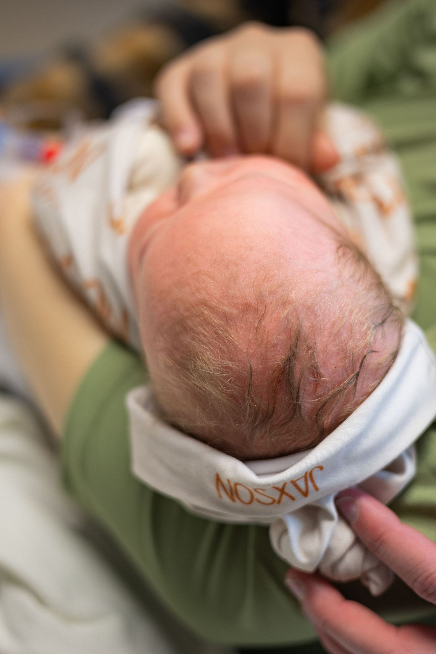 Close-up of a newborn baby's head wearing a white hat in a hospital setting.