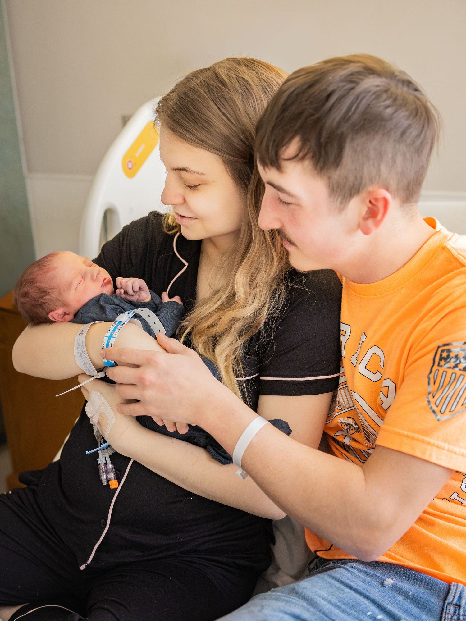 Young couple sitting together in hospital room smiling at their newborn baby after birth.