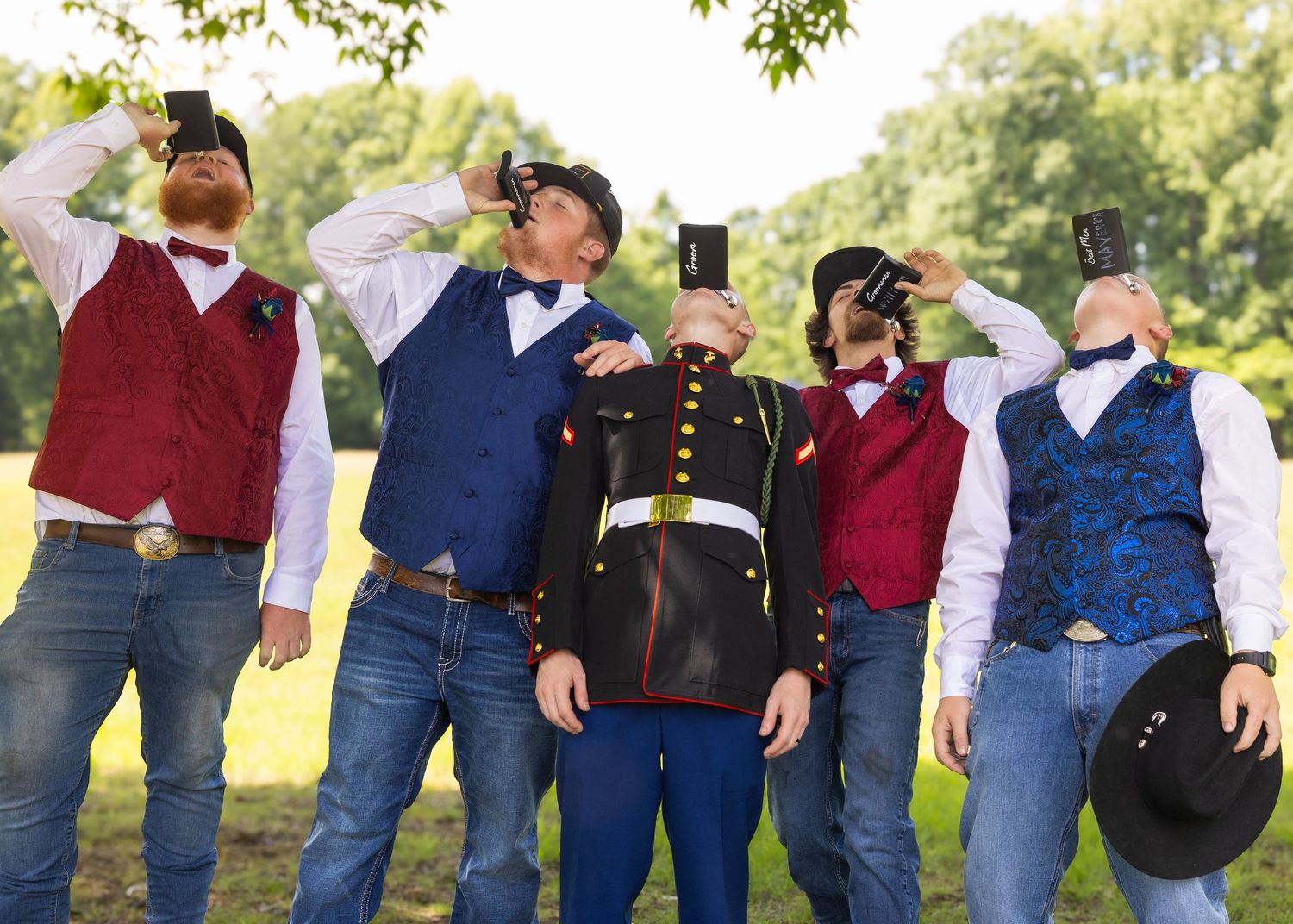 Five men in formal attire with vests and bow ties humorously cover their faces with phones outdoors.