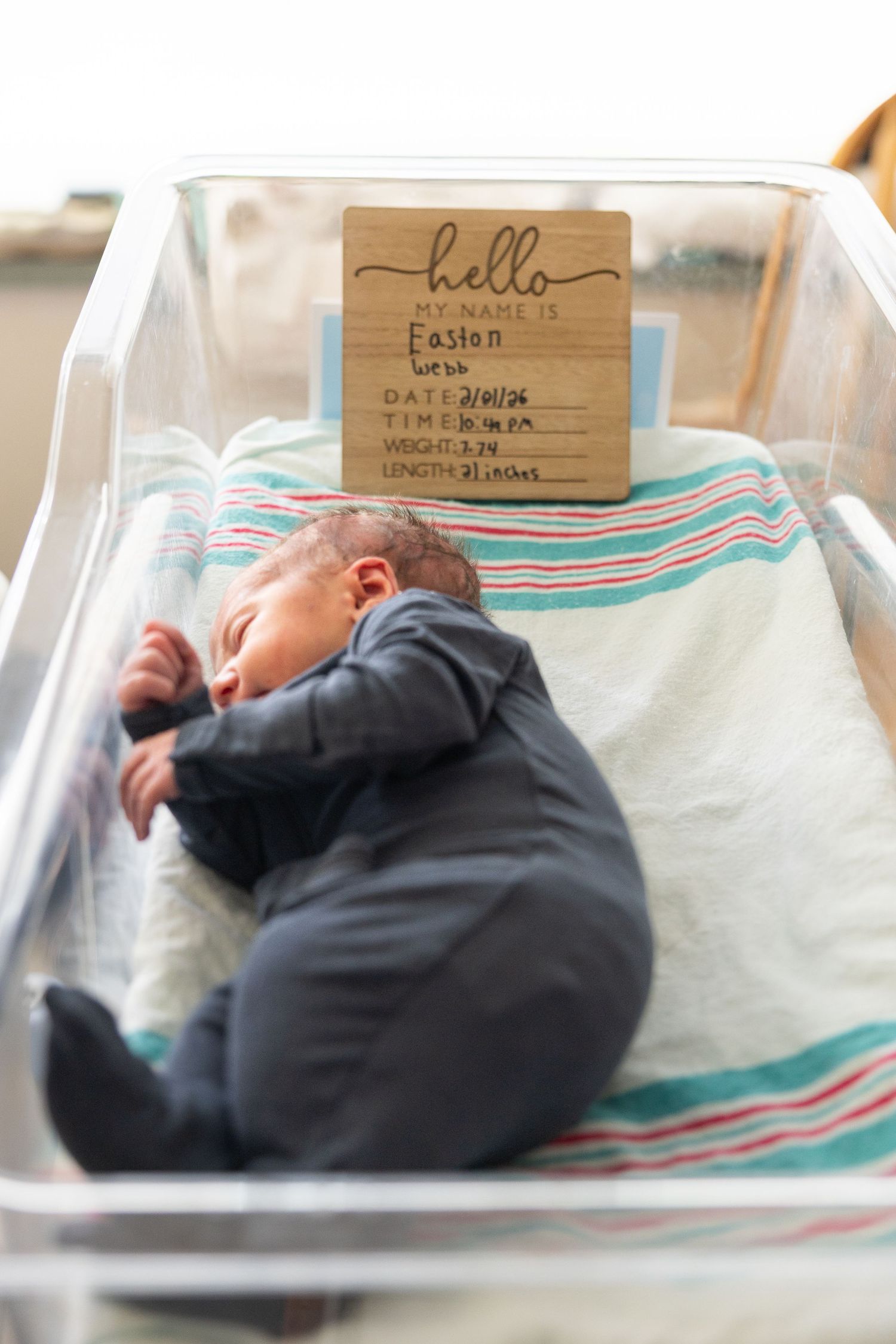 Newborn baby named Easton sleeping in a hospital bassinet with a wooden birth announcement sign.