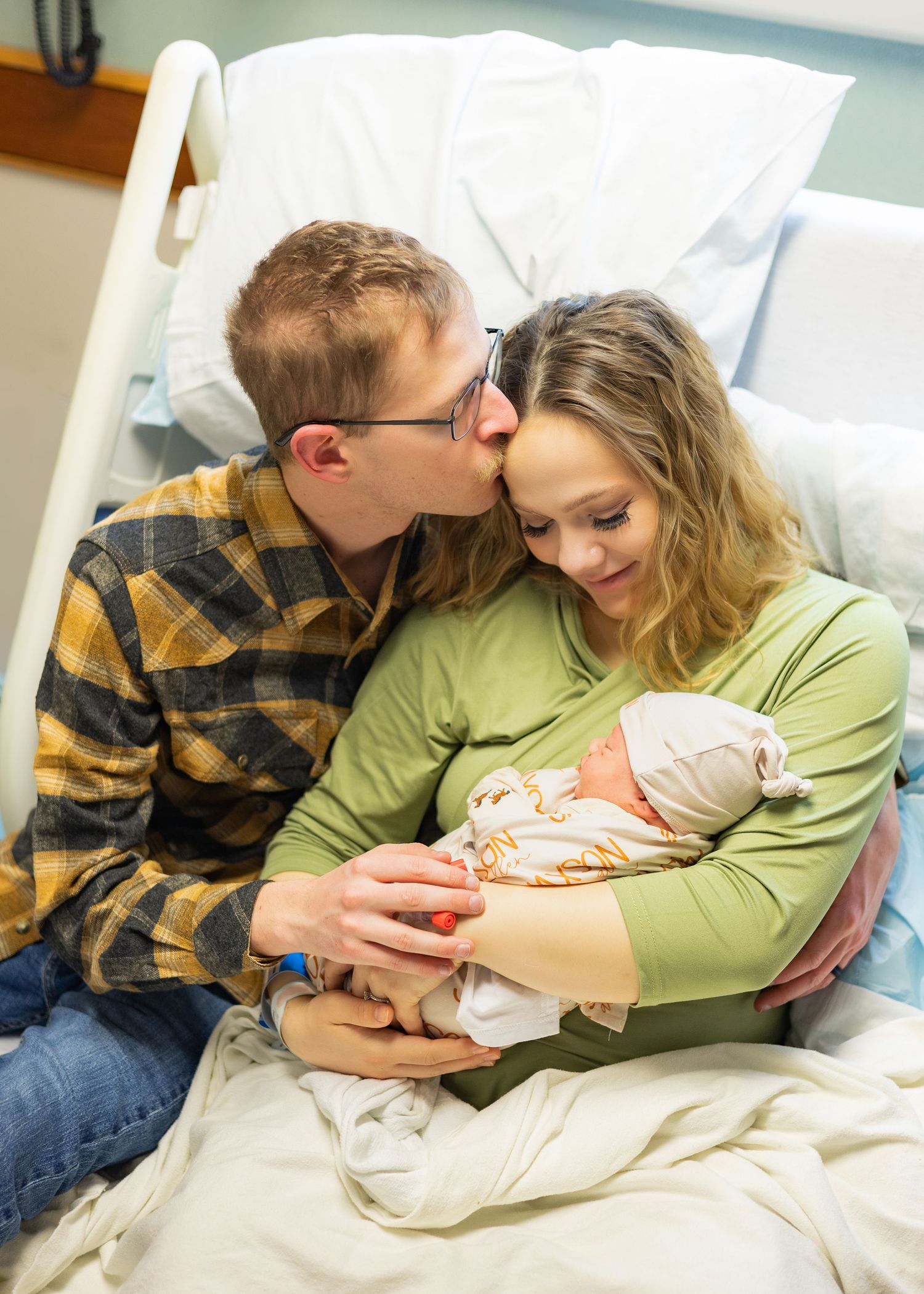 New parents kiss and cuddle their newborn baby in a hospital room after delivery.