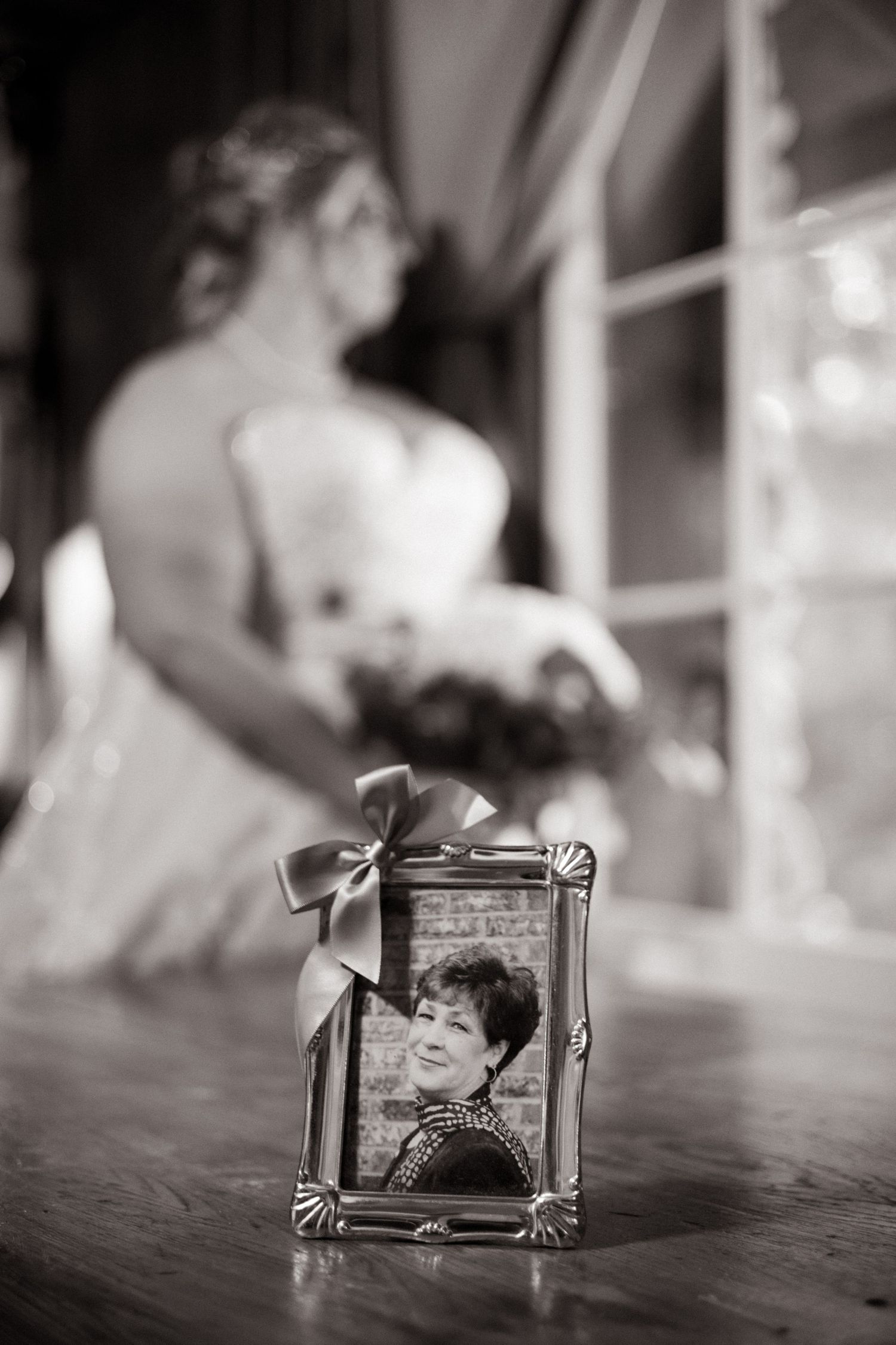 Framed memorial photo of loved one displayed on table with bride blurred in background.