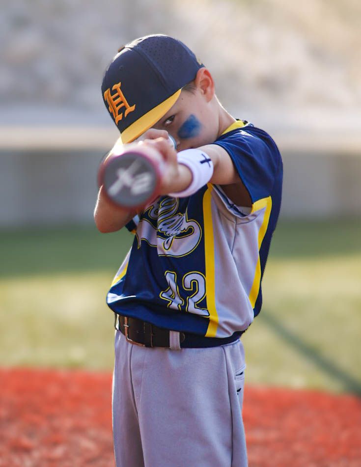 Young baseball player in navy uniform number 42 pointing bat toward camera on red field.