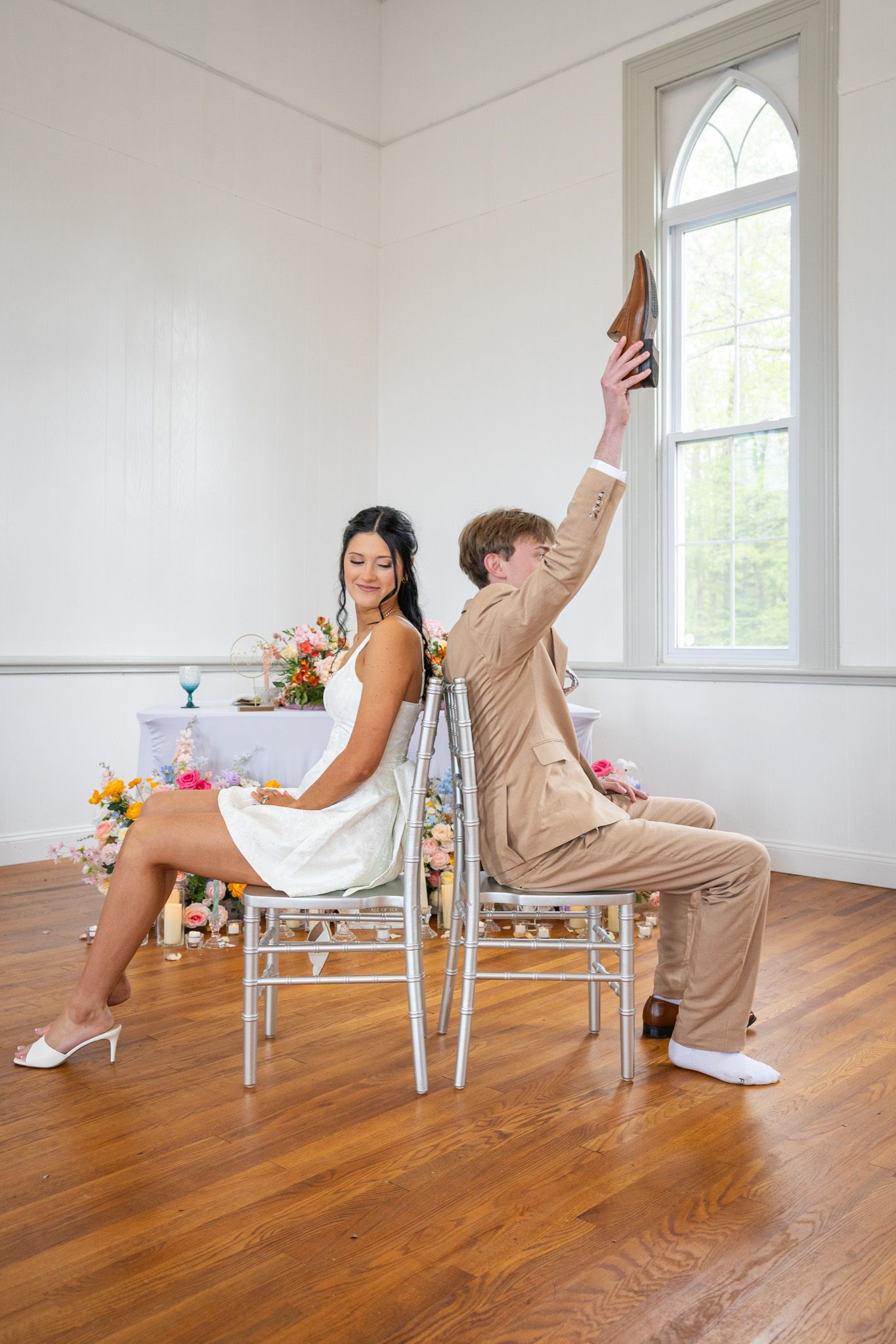 Bride and groom play the shoe game at their wedding reception in a bright white chapel venue.
