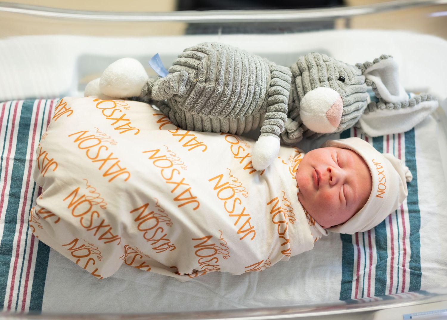 Sleeping newborn baby swaddled in personalized Jaxson blanket with a stuffed elephant toy.