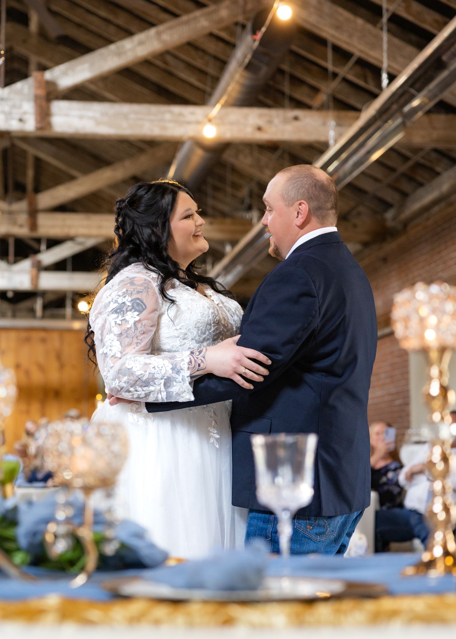 Bride and groom sharing first dance in rustic wedding venue with exposed wooden beams and elegant decor.