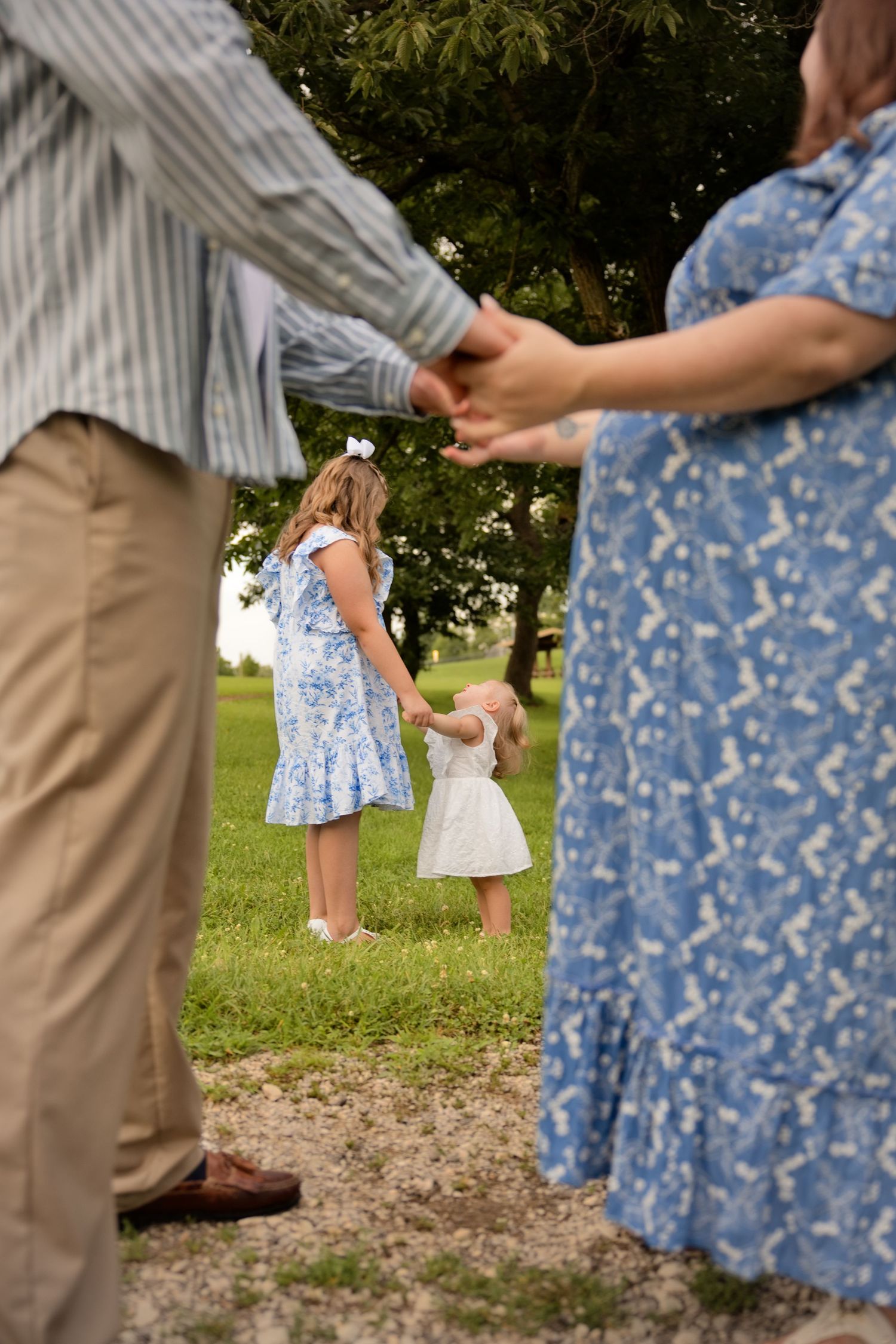 Family holding hands outdoors in a park, two girls in blue dresses with pregnant mother and father.