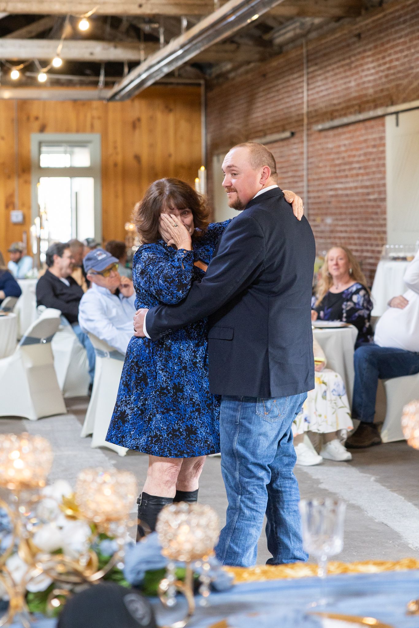 Emotional mother and son share a dance at wedding reception in industrial brick venue.