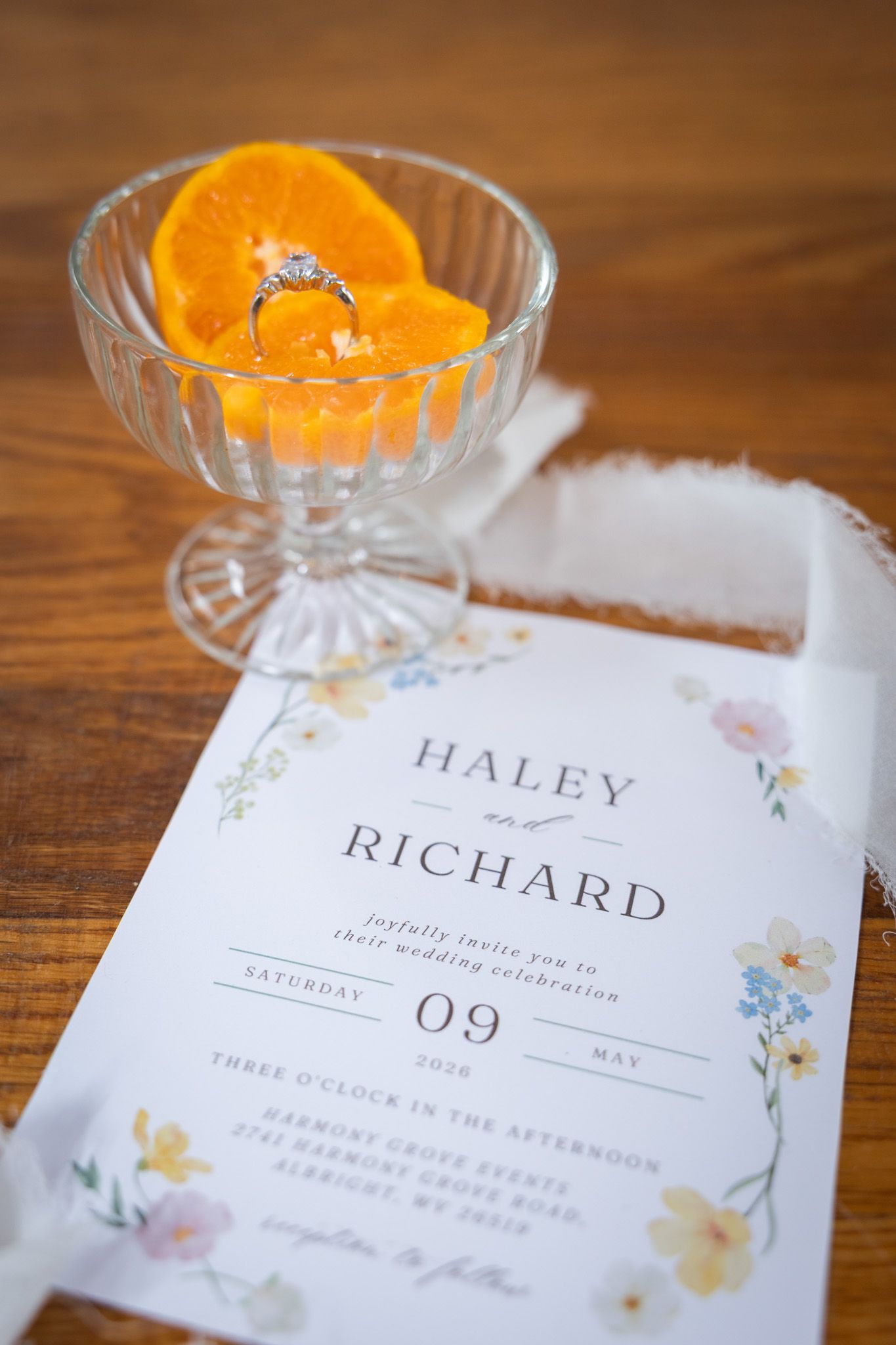 Wedding invitation for Haley and Richard with diamond ring resting on orange slices in glass dish.