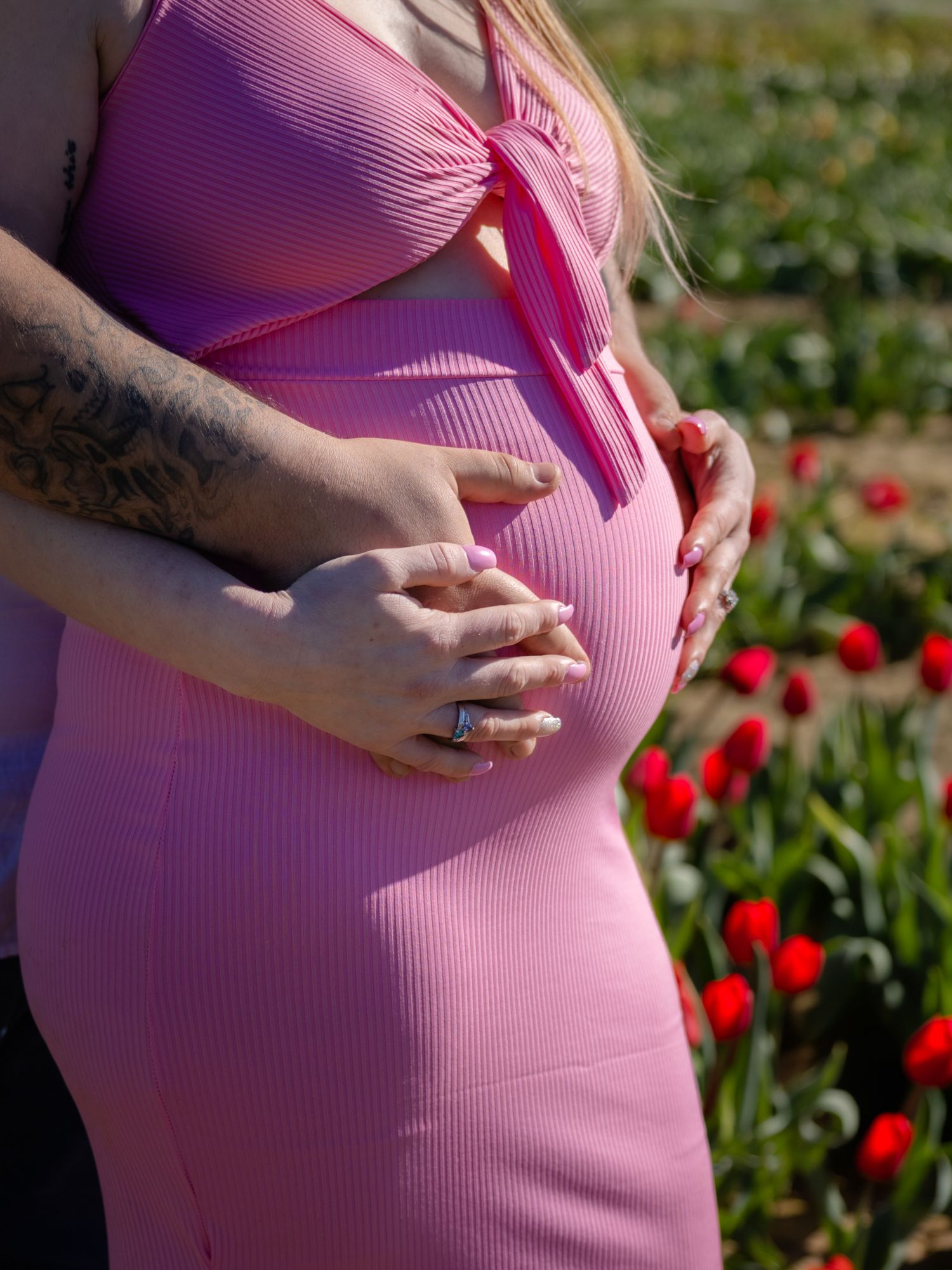 Pregnant woman in a pink ribbed dress cradling her baby bump in a vibrant tulip field.