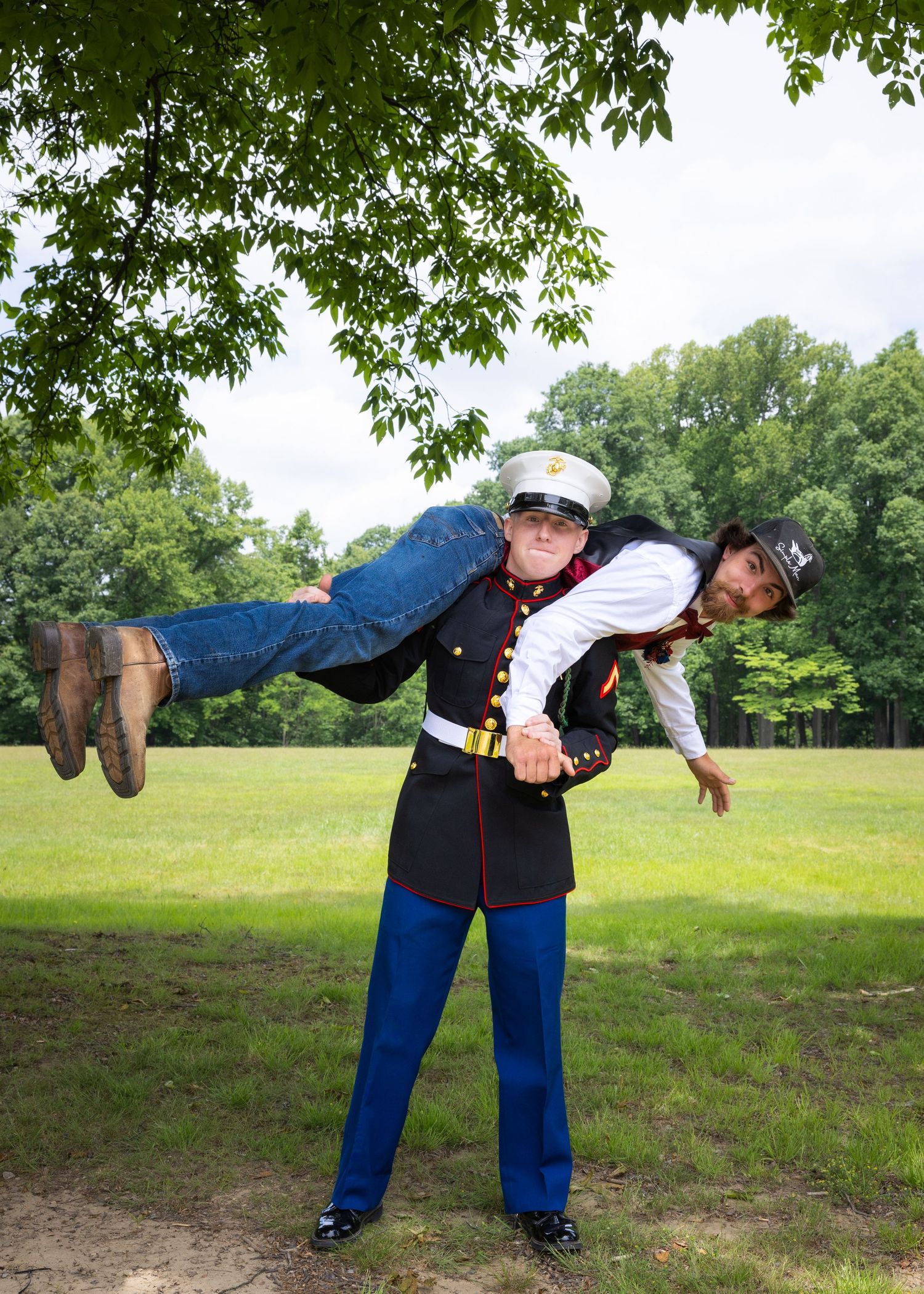 Marine in dress uniform carrying a person over his shoulder in a park setting.