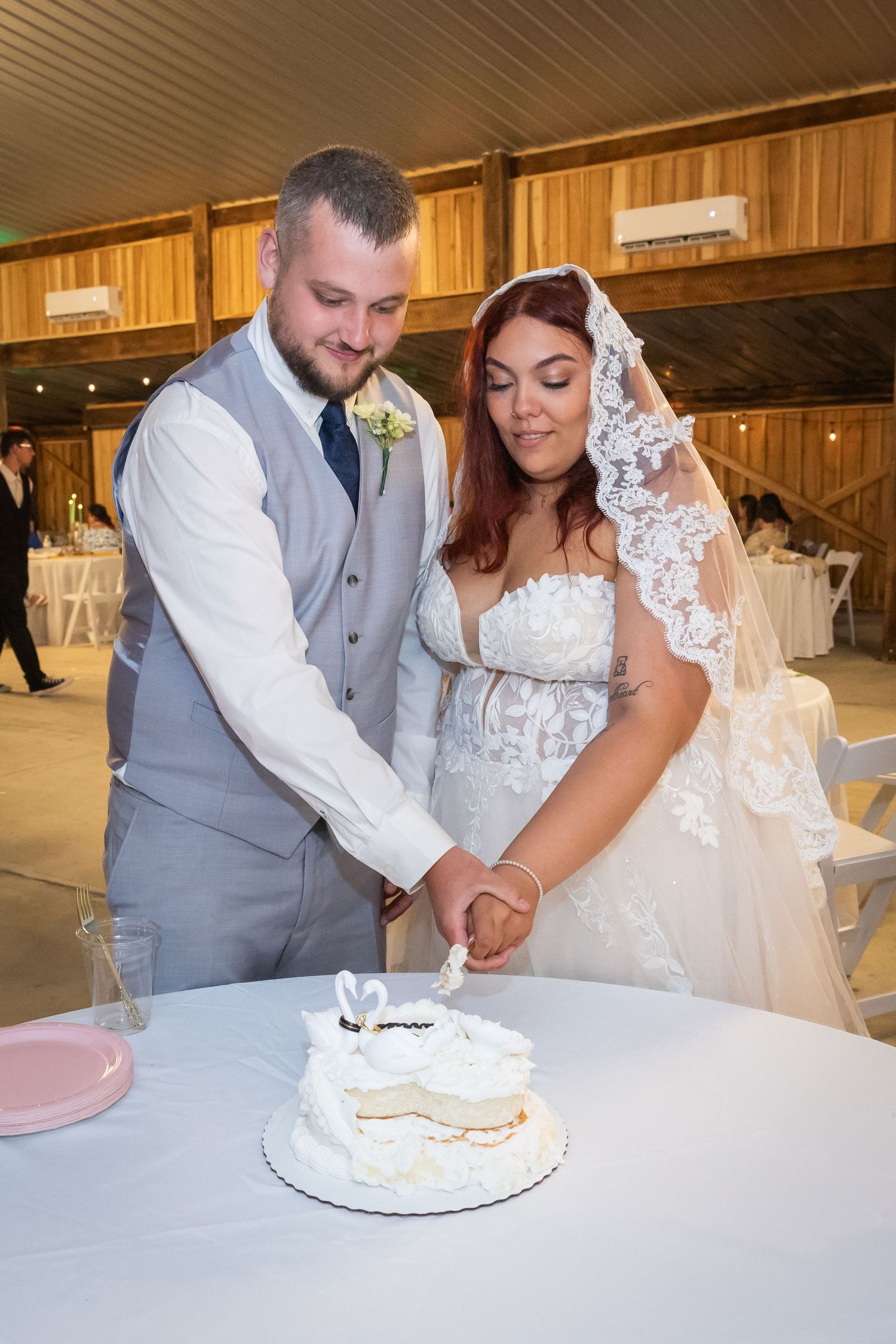 Bride and groom cutting their white wedding cake together at a rustic barn reception venue.