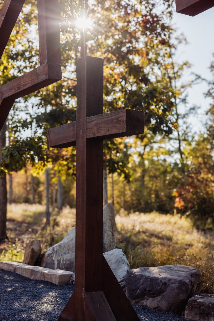 Rustic wooden cross glowing in sunlight surrounded by autumn trees and rocks at an outdoor wedding venue.