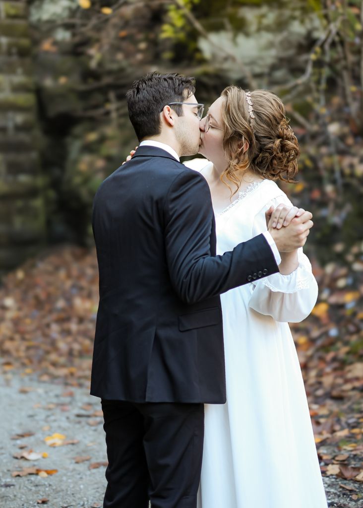 Bride and groom sharing a romantic kiss outdoors in autumn, dressed in white gown and black suit.