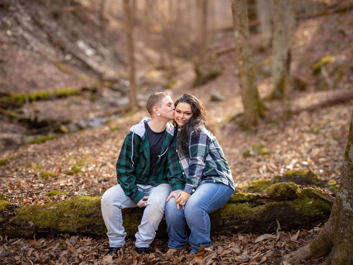 Couple sitting on a moss-covered log in an autumn forest, sharing a tender moment.