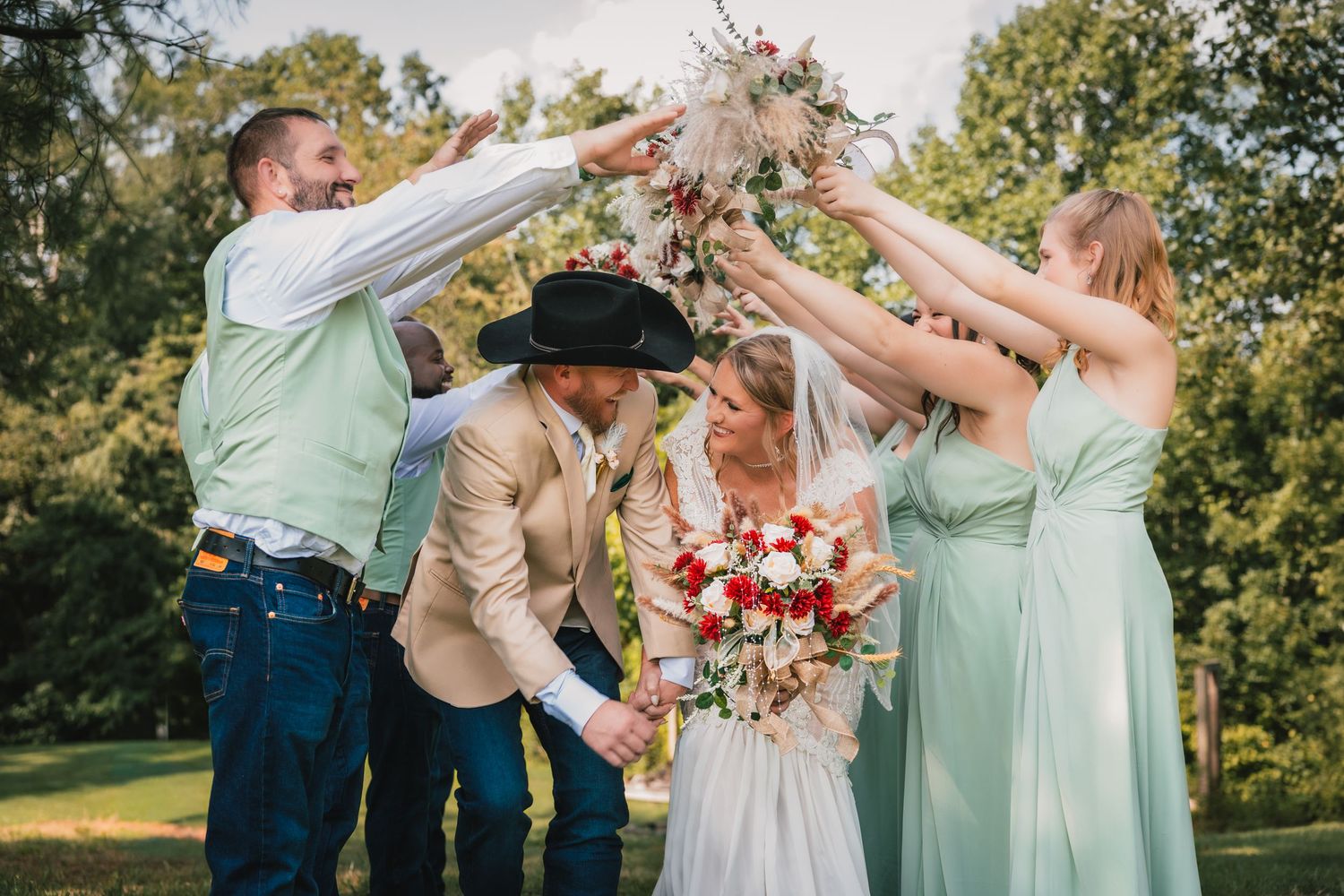 Bride and groom in cowboy hat celebrate with wedding party in mint dresses and sage suits outdoors.