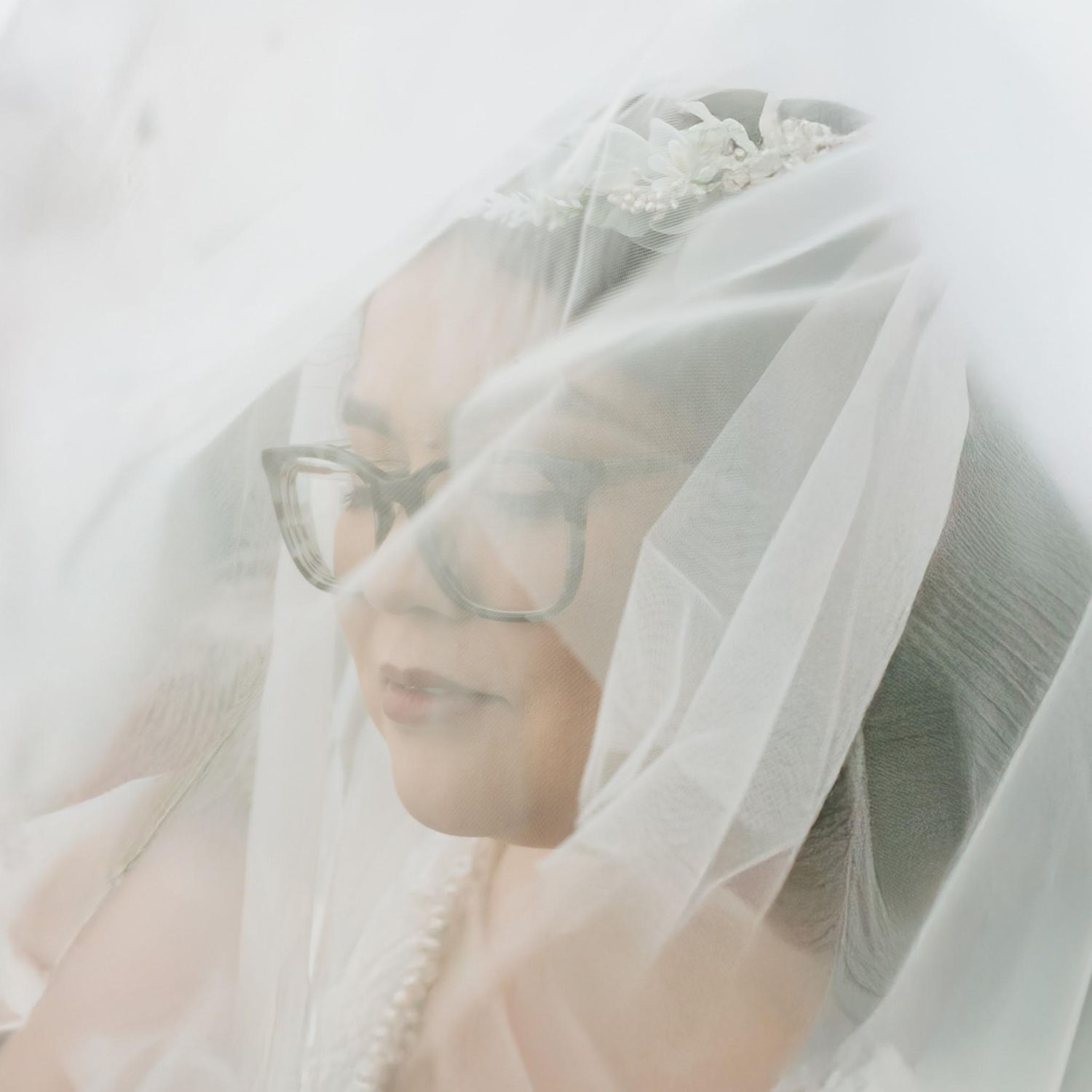 Close-up portrait of bride wearing glasses beneath a soft flowing white wedding veil.