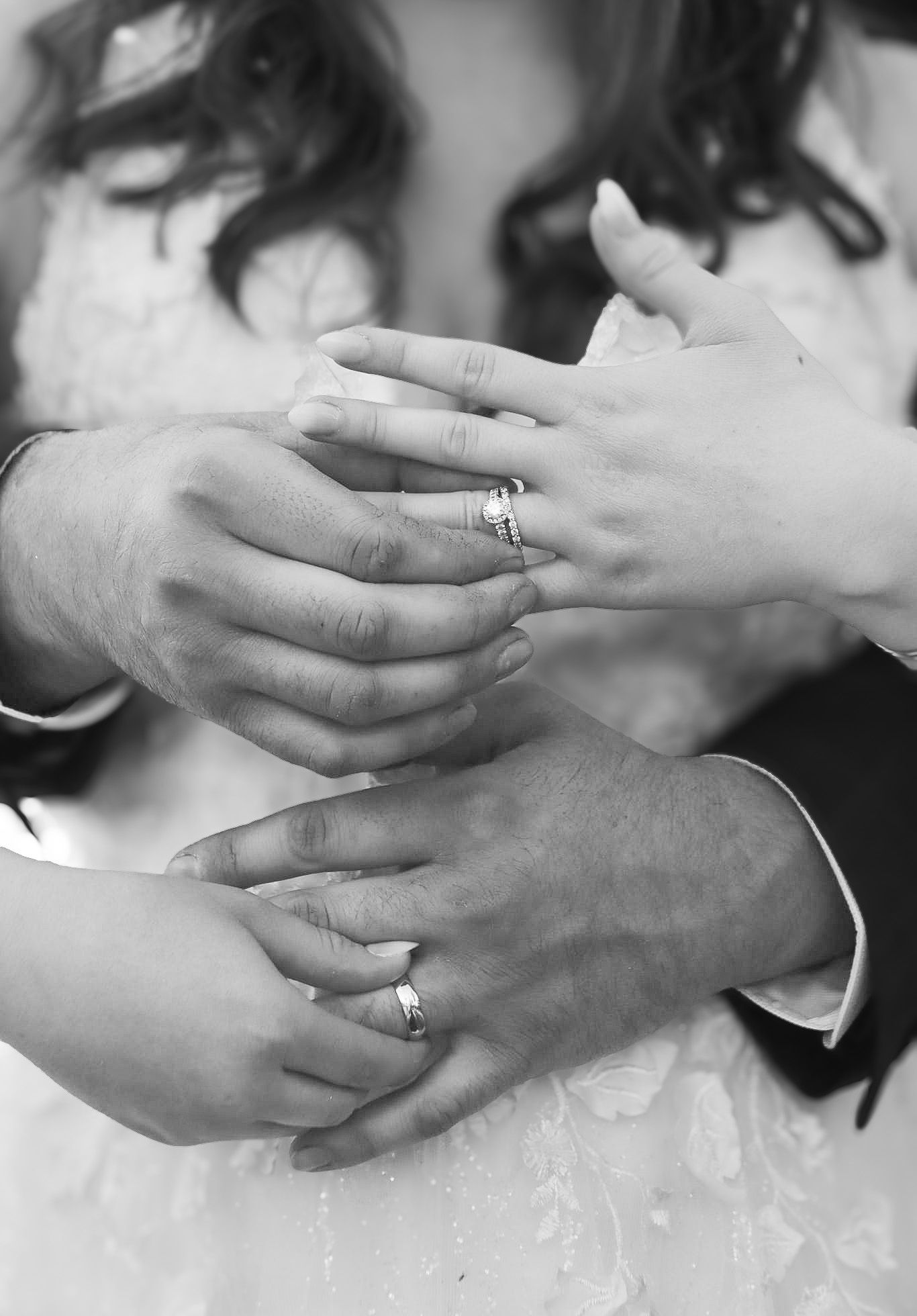 Black and white close-up of bride and groom hands displaying wedding and engagement rings.
