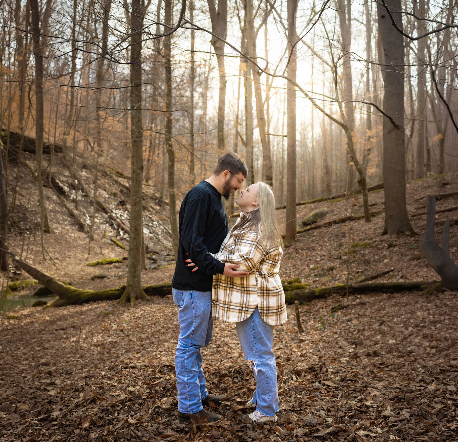 Young couple sharing a kiss in sunlit autumn forest surrounded by fallen leaves.