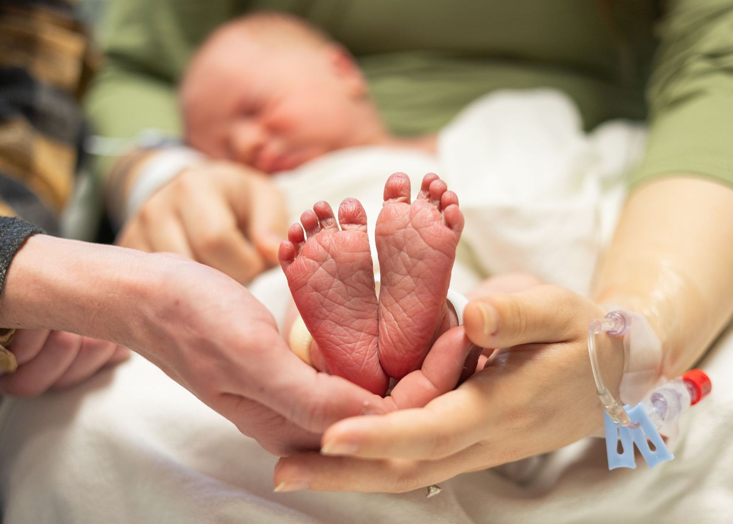 Parents gently holding tiny newborn baby feet in the hospital after birth.