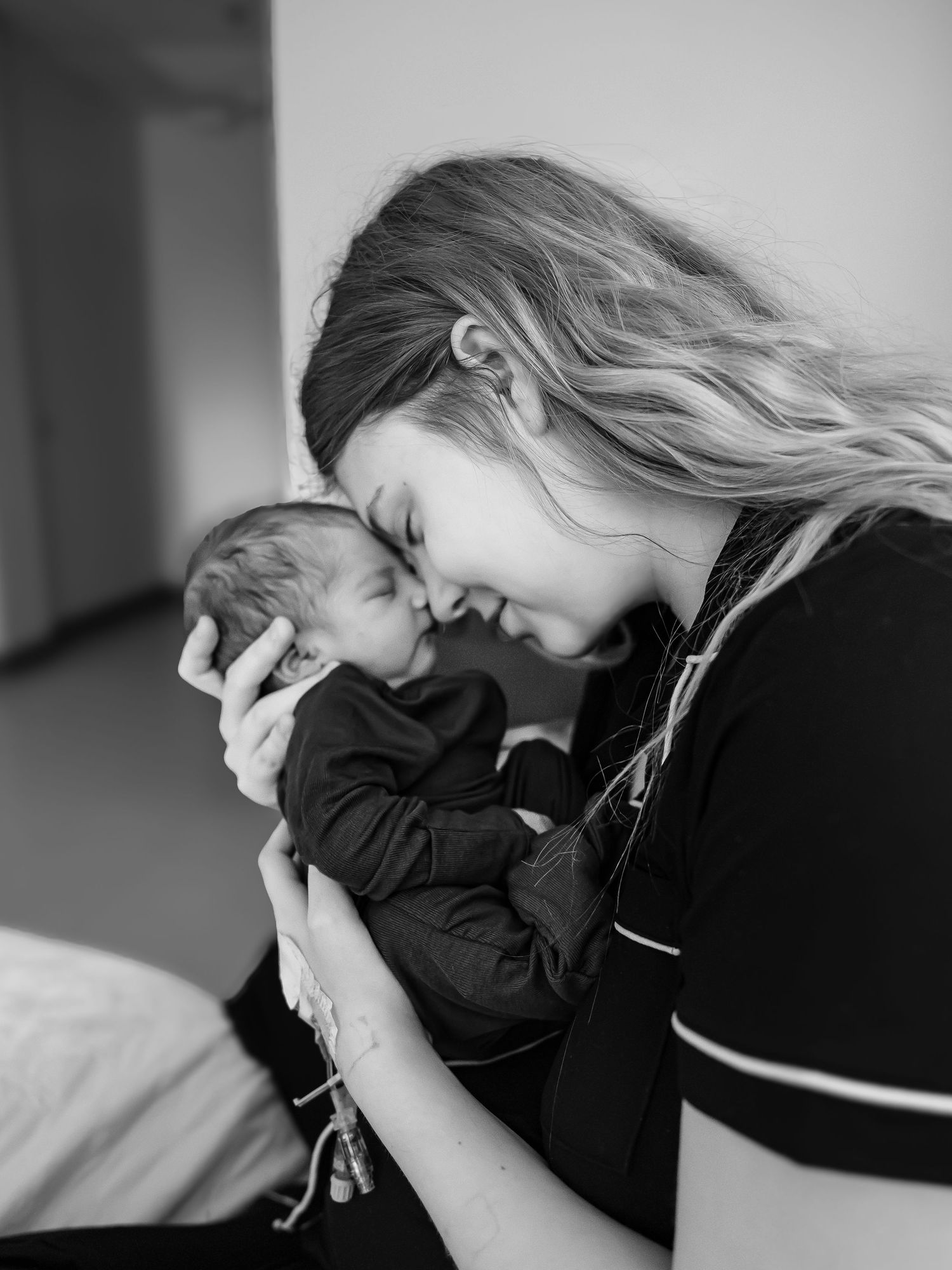 Black and white photo of a young mother tenderly holding her newborn baby close to her face.