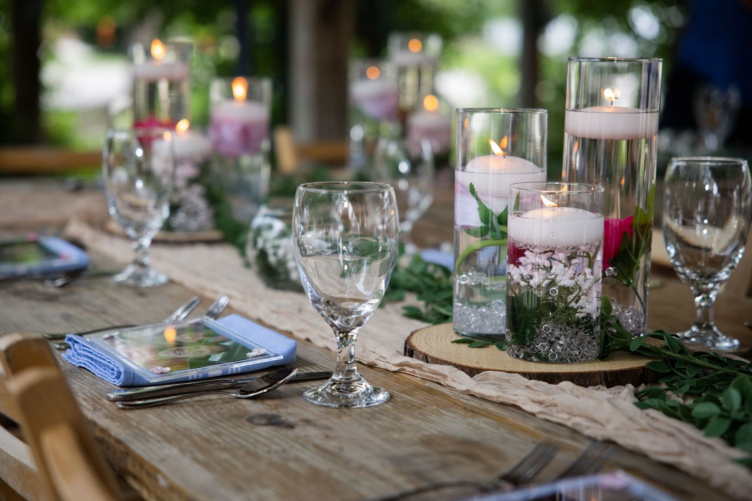 Elegant outdoor wedding reception table with floating candles, crystal glasses, and floral centerpieces on a rustic wooden table.