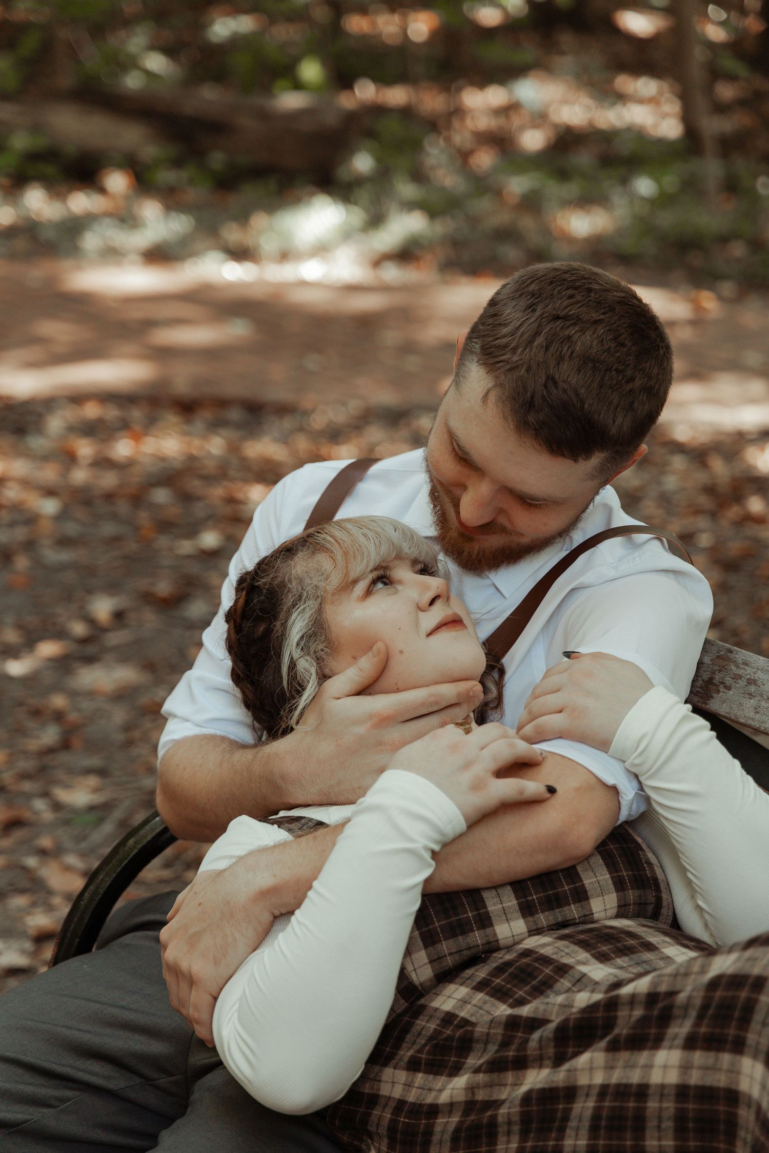Romantic couple embracing on a bench in the woods, man with beard holding woman tenderly in black and white.