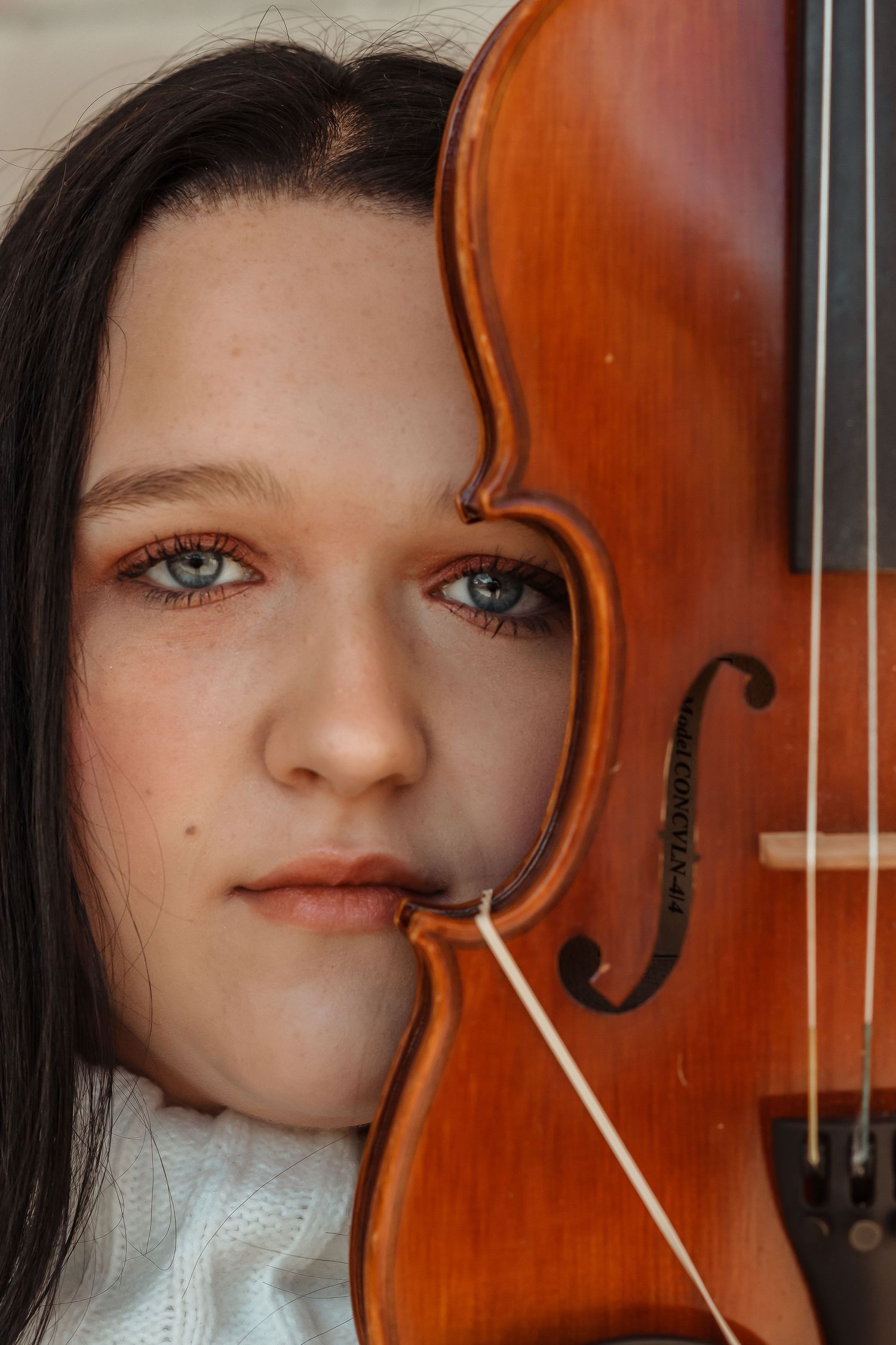 Close-up portrait of young woman with blue eyes half-hidden behind a wooden violin.