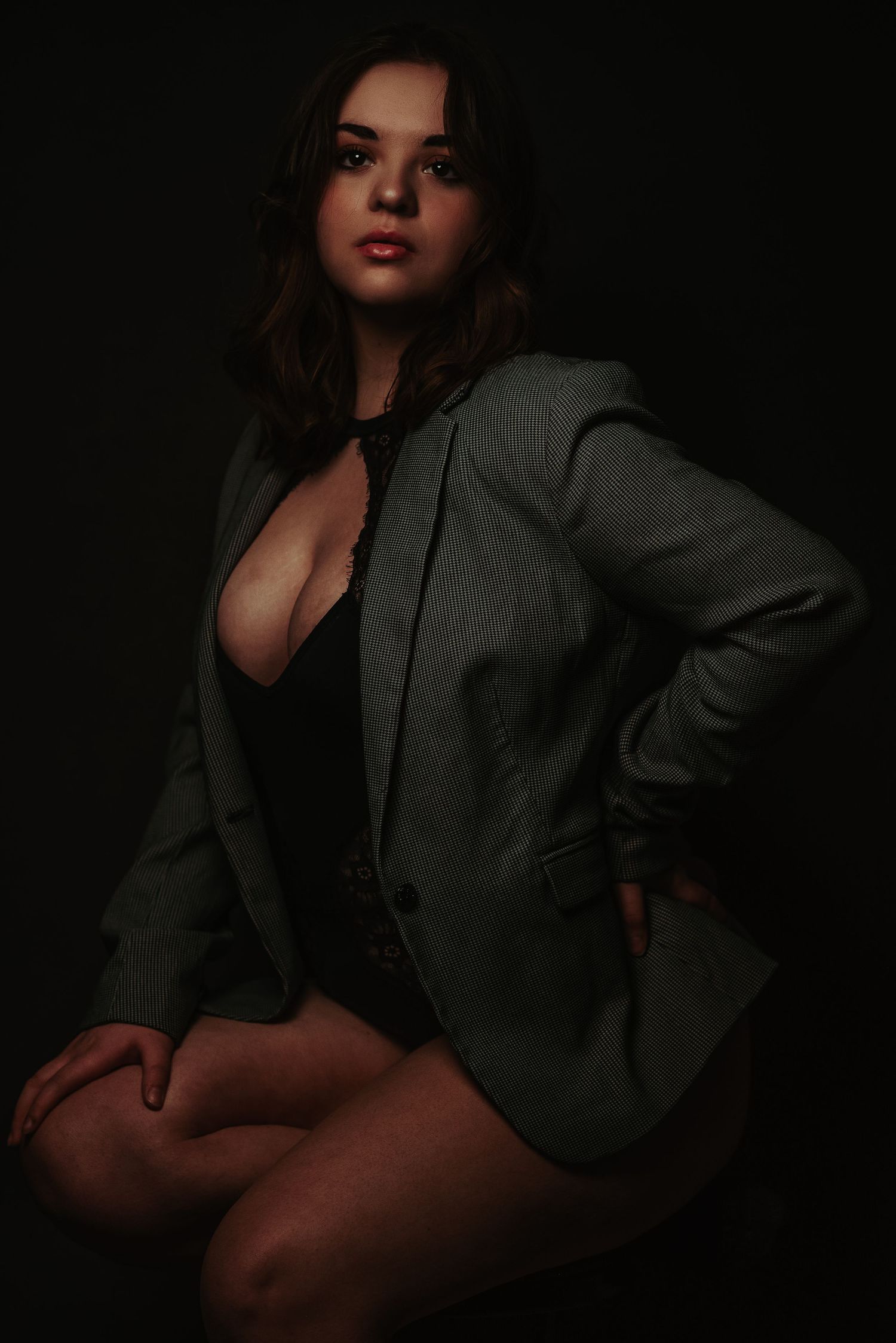 Woman in green blazer and black bodysuit posing in dark studio lighting.