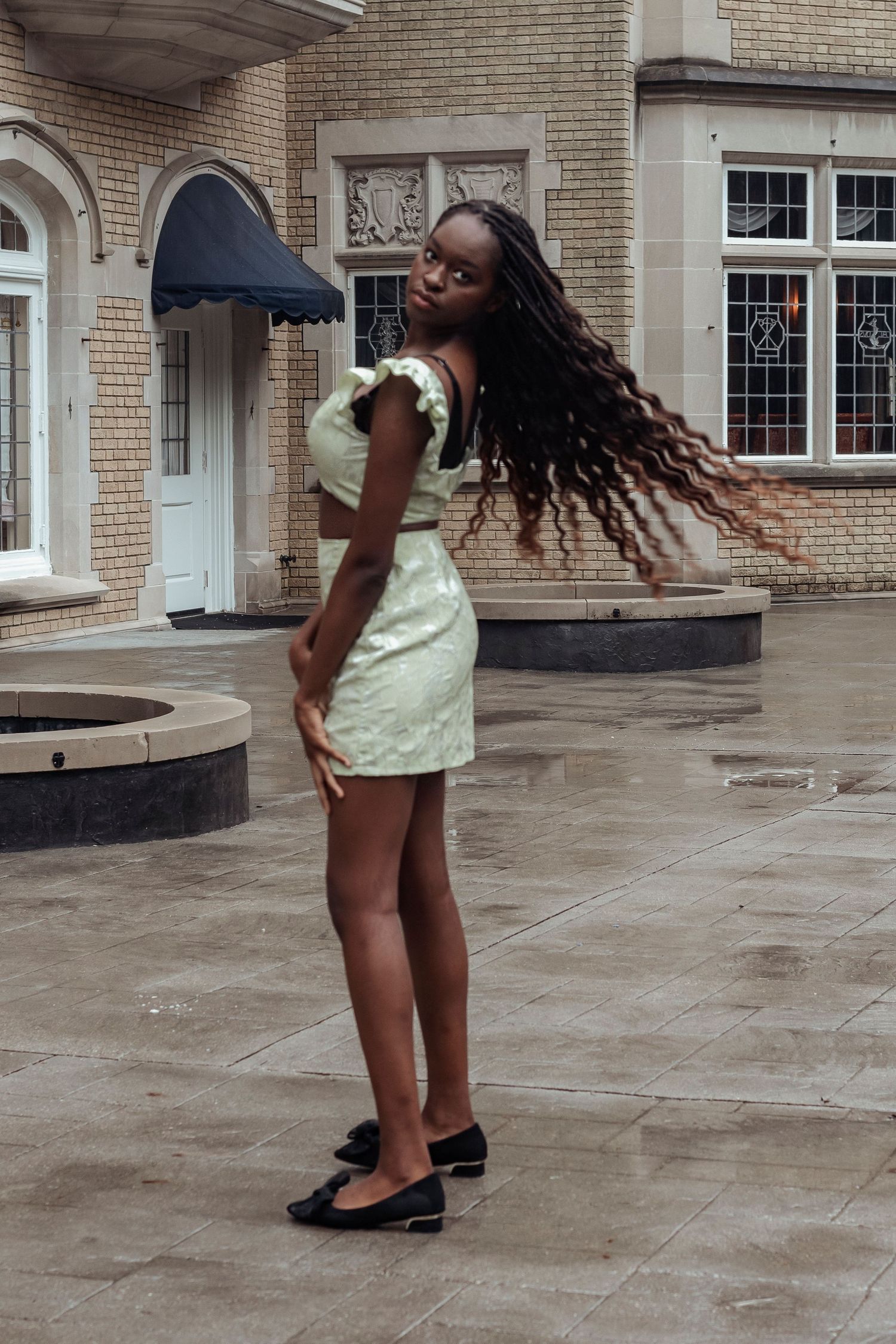 Young woman in mint green mini dress with long braids posing outdoors at historic building.