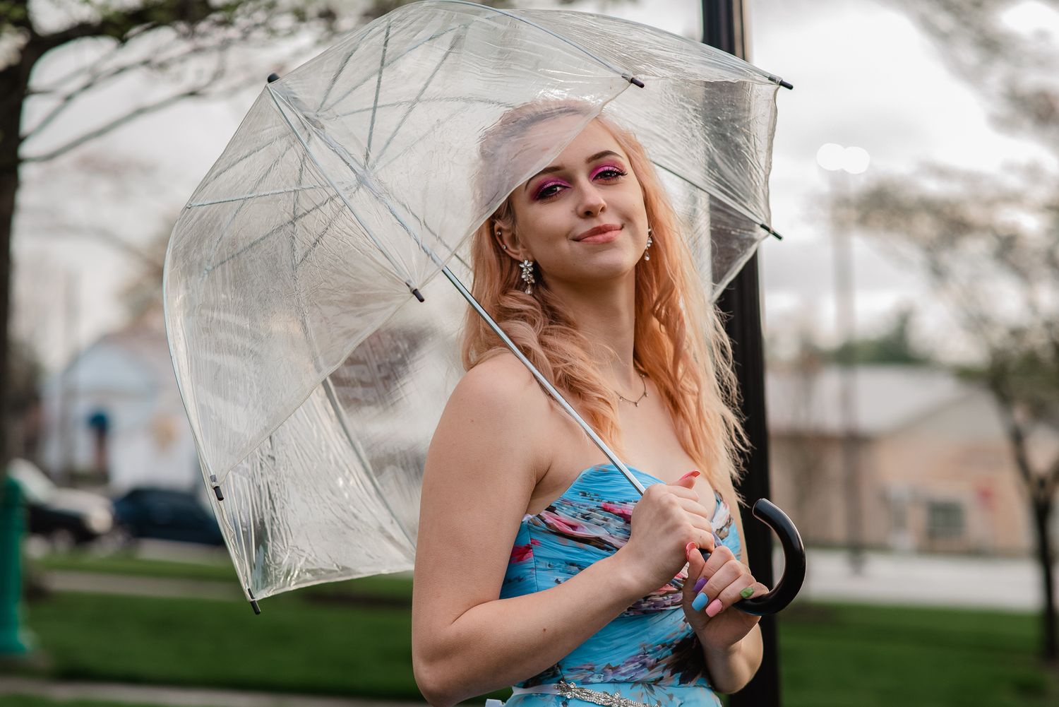 Young woman in blue dress holding clear bubble umbrella outdoors on a cloudy day.